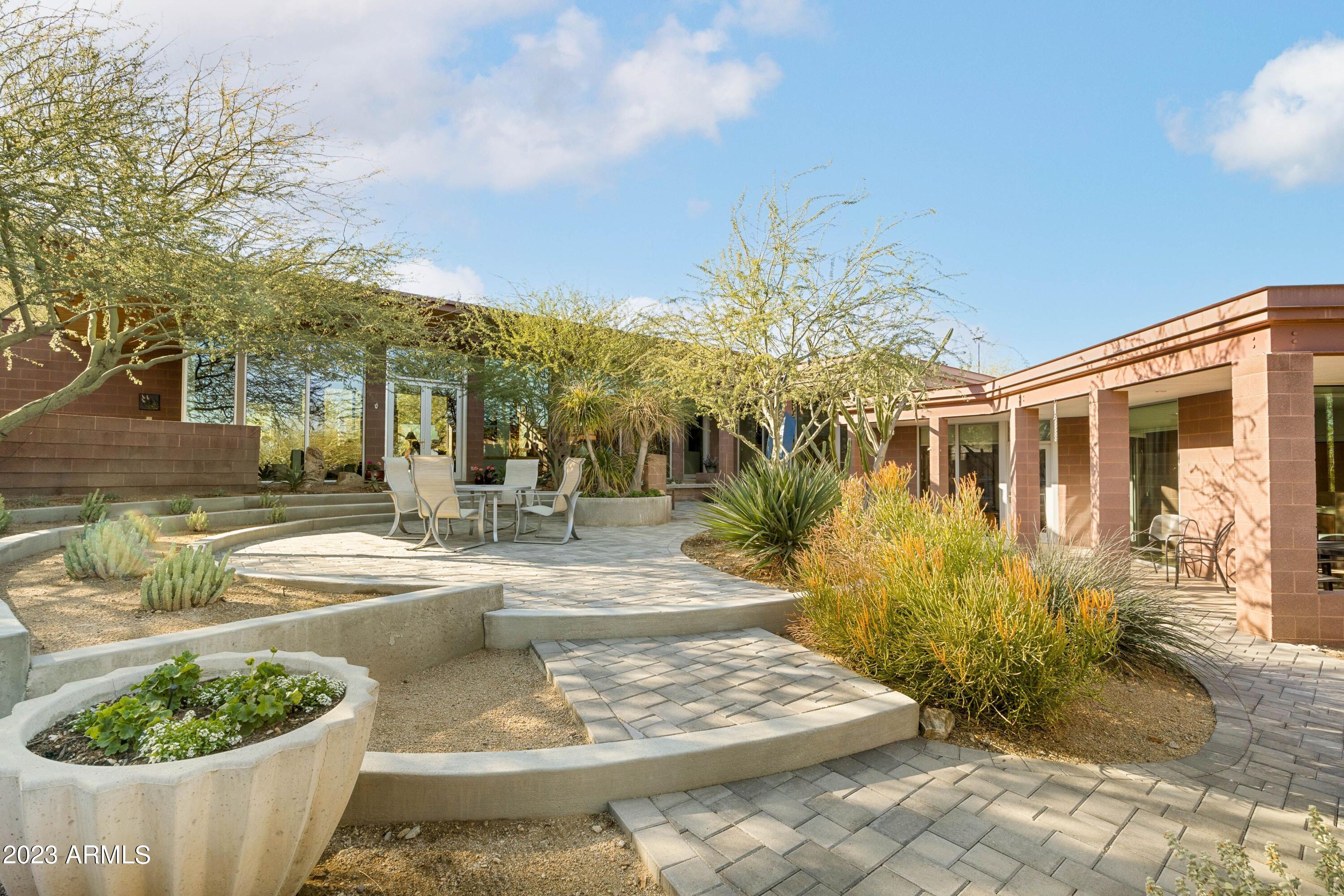 On the Edge of a Mountain Preserve.
Secluded, Serene Sanctuary. 
The architecture celebrates the special qualities of the property.  Primary bedroom, family, kitchen, dining, living, office, relate to each other in a linear sequence on a single level that integrates with the natural landscape, following the contours of the desert. The plan orientation allows natural light to flow from both sides to all the main spaces under the metal butterfly roof that lifts to reveal the mountain preserve peaks as well as the distant city lights on the north horizon, Comfortable guest rooms embrace a large but private front courtyard,, A spacious three-car garage, with direct access to the kitchen through storage discreetly positioned away from the entry experience & guests arrival & parking. The broad twelve-foot overhang of the butterfly roof provides patio opportunities while shielding the interior from summer sun and letting winter sun in to warm the interior masonry, concrete, and quartzite. On the north, the roof protects the energy-efficient glass corridor looking over the front patio toward a horizon of distant city lights. The butterfly shape harvests rain water through long scuppers into concrete cisterns that are fountains during rain and holding ponds for the natural blooming landscape.
 
Highlighted features:
 
- The unique floor plan works for entertaining yet comforts day-today living and privacy.
- Quiet primary bedroom with large bath and two closets. 
- Large kitchen with high-end newer appliances, custom Maple cabinetry, & granite counters opens to family gathering and access to dining room and patios.
- Special garden room/bedroom #2 at east end.
- Carefully detailed wood ceilings.
- Colored concrete flooring with quartzite insets between the structural columns.
- Separate guest rooms, connected by a shaded gallery, can be used as two comfortable guest suites with kitchenette and private access. 
- Exterior colors of crafted masonry blend with the setting and extend throughout the interior, expressed in the fireplaces and structural columns that articulate the living spaces.
-Zoned, high efficiency air conditioning.
-New West Anderson windows.