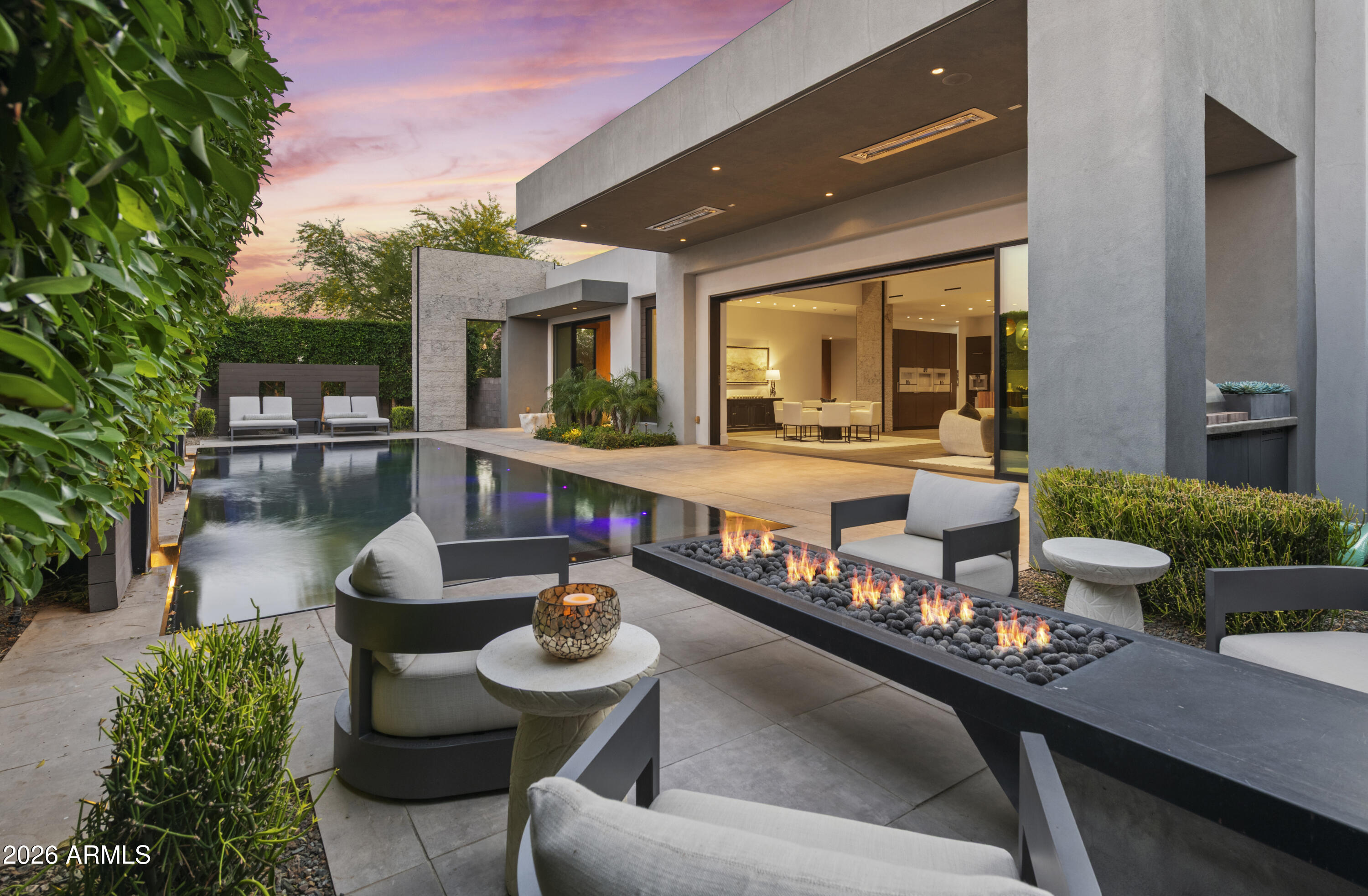 Located within minutes of everything desirable, this Move-in-ready ultra-luxury lock and leave home with modern architecture awaits you. A dramatic double-height glass entry framed by floor-to-ceiling windows opens to a stone-clad foyer and soaring interiors where sight lines extend through the home into the low-maintenance backyard.
Designed as the heart of the home, the ambiance blends interior and exterior living with ceramic pavers, a fireplace, lap-pool, and retractable blinds, while expansive glass walls connect surrounding spaces in breathtaking fashion. The chef's kitchen features a waterfall island, sleek European frameless cabinetry, and a full suite of Gaggenau appliances, complemented by a spacious pantry and elegant dining bar designed for entertaining. The great room is anchored by a floor-to-ceiling stone fireplace and sound-absorbing ceiling.
The primary suite offers a sophisticated retreat with walls of glass opening to the courtyard and a spa-inspired bath featuring floating vanities with Crystal Quartz, a freestanding soaking tub, and a zero-entry rain shower.
The finished lower level introduces a dramatic media lounge, wet bar with Thermador refrigeration, powder room, and two private guest suites.
The captivating loft lives as a 5th suite or private office expanding onto a rooftop patio with mesmerizing Camelback Mountain Views. 
Modern convenience is seamlessly integrated through Savant home automation, Lutron lighting, and app-controlled Daikin HVAC. The garage features epoxy flooring, custom storage, a workspace counter, and EV charging station.
Outdoors, the resort-style backyard offers a heated patio, infinity-edge pool, outdoor kitchen with built-in BBQ and beverage refrigerator, gas fire pit, and serene landscape lighting.