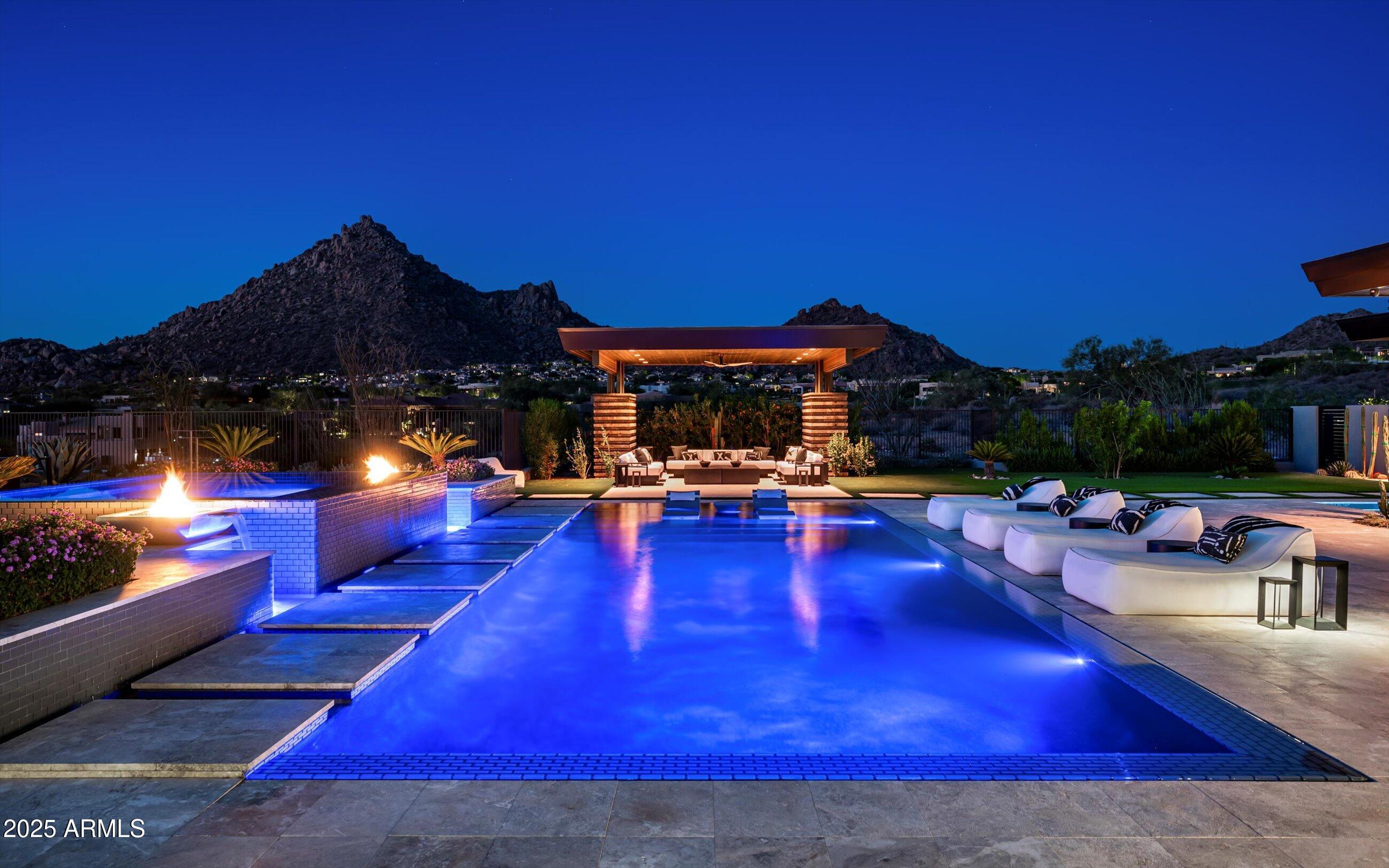 A true showpiece in the gated enclave of Legend Canyon, this 7,063 sq. ft. estate was designed by Tom Mooney and built by Modern Splendor Homes. Perfectly positioned against the backdrop of Pinnacle Peak and the Troon mountains, it blends timeless architecture with next-level innovation. The main home offers 4 en-suite bedrooms and 4.5 baths, paired with an attached 1 bedroom / 2 bath casita, complete with a full kitchen—ideal for guests, multigenerational living, or private retreat. A private lounge just off the dining room offers an inviting space for quiet conversation with your dinner guests. Cutting-edge features include a fully integrated Josh AI system with whole-home voice control and over $120,000 in Ketra lighting, delivering customizable ambiance that shifts naturally throughout the day. The backyard is built for entertaining-  two pools, a spa, water features, ramada and expansive covered patios create the ultimate private desert retreat. Enjoy the big game from multiple vantage points whether under the covered patio or from the pool, with a retractable, swivel-mounted screen that rises seamlessly from the ground. Motorized telescoping doors and open seamlessly to the outdoors, framing breathtaking views and offering the best of Arizona indoor-outdoor living. Finishes like Black Canterra stone, Leathered Granite, Sierra Pacific doors and windows, motorized shades, custom Ted Bradley light fixtures, and a chef's kitchen with premier appliances elevate every detail. Car enthusiasts will appreciate the impressive four-car garage, fully temperature-controlled to protect vehicles year-round.  Powered by solar energy, the home helps keep electric bills low while offering sustainable efficiency. Featured in Build Magazine, this estate represents luxury, technology, and lifestyle at the highest level.