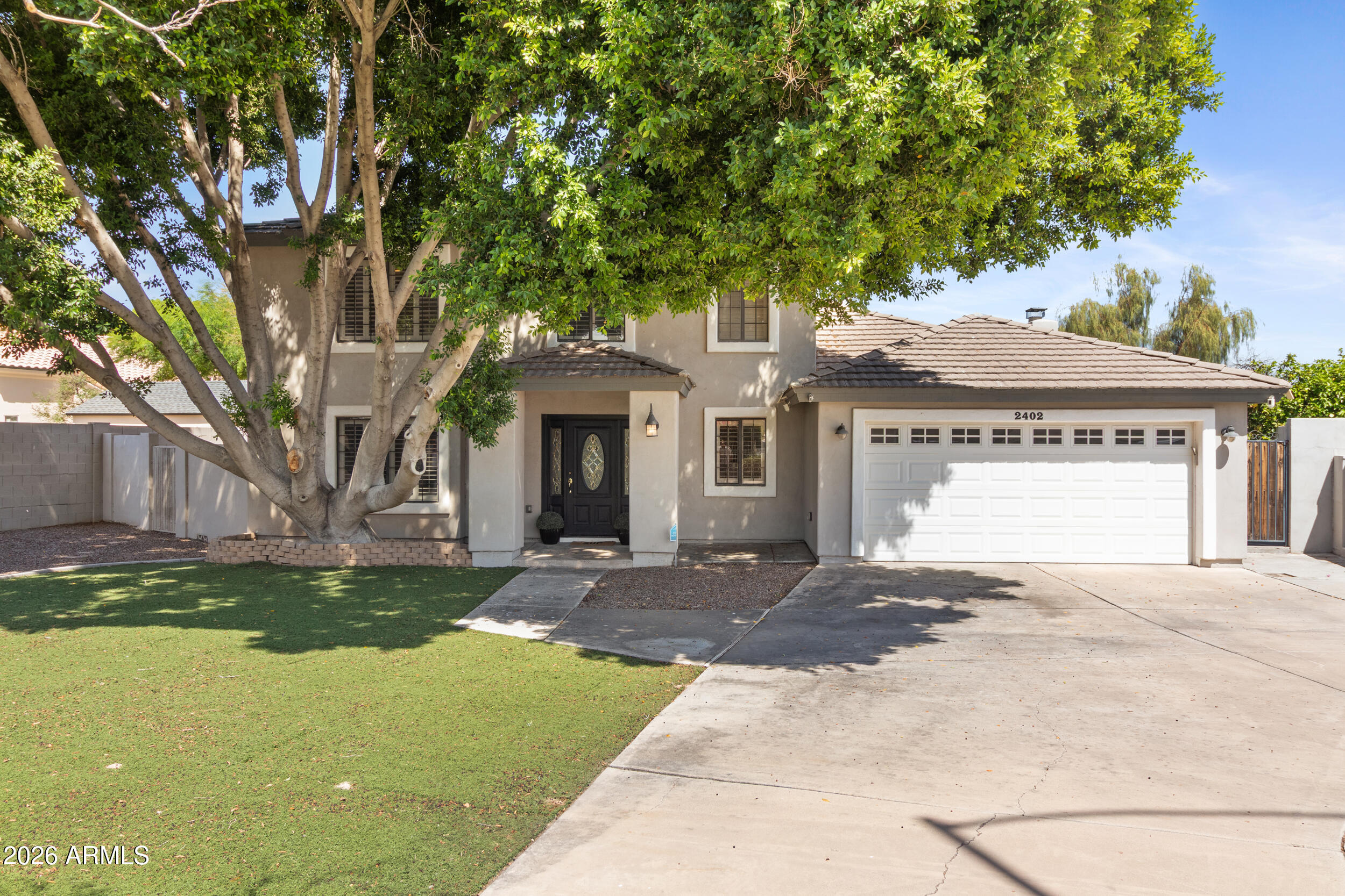 Welcome to 2402 E Kramer Circle, Mesa, AZ 85213, a stunning designer 5-bedroom, 3.5-bath home nestled on a prime cul-de-sac lot in the heart of Northeast Mesa's Citrus Highlands neighborhood. From the moment you arrive, this home impresses. A canopy of mature trees frames the lush artificial turf front yard, and a bold black front door with leaded glass sidelights signals the elevated style found throughout. The aerial view tells the full story: an expansive, private lot with room to live, entertain, and breathe. Inside, the grand two-story foyer sets the tone with custom herringbone tile, designer wainscoting, dual crystal chandeliers, a sliding barn door, and a sweeping staircase with dark wood railings and white spindles. Every detail has been thoughtfully curated. The open-concept main living area is warm, bright, and incredibly spacious. The great room anchors around a dramatic floor-to-ceiling white painted brick fireplace with shiplap accent walls, a stunning focal point that feels both cozy and stylish. Wood-look tile flooring flows throughout most of the main level, with carpet in two downstairs bedrooms. The fully reimagined kitchen is a showstopper. White shaker cabinetry extends to the ceiling, complemented by a built-in wine rack, stainless steel appliances including a double wall oven, a center island with quartz countertops and counter-height seating, mosaic tile backsplash paired with sculptural pendant lighting. It opens directly to the dining area and backyard, making entertaining seamless. Just off the kitchen, a beautifully finished butler's pantry features cabinetry, quartz counters, subway tile backsplash, and glass shelving, perfect for hosting. A shiplap accented built-in home office nook with custom desk and cabinetry adds function without sacrificing style. A chic powder bath completes the main floor. Two downstairs bedrooms offer flexibility, with one ideal for a guest suite, home office, or playroom. Upstairs, the primary suite is spacious and well-appointed. The partially renovated en suite bath features floor-to-ceiling marble look tile, an existing corner soaking tub surrounded by glass block windows, a frameless glass walk-in shower with mosaic tile flooring, and a dual sink quartz vanity. The massive walk-in closet is fully customized with double hang rods, built-in shelving, dedicated shoe display, and soft close drawers. The backyard is an entertainer's paradise with lush artificial turf, a sweeping curved concrete pathway, large covered patio with ceiling fans, gas grill area, a charming detached shed, multiple lounge areas, mature citrus trees, and full block wall privacy. Low maintenance with high impact. Top rated schools including Hermosa Vista Elementary and just minutes to the Loop 202, shopping, and dining. This is Northeast Mesa living at its finest.