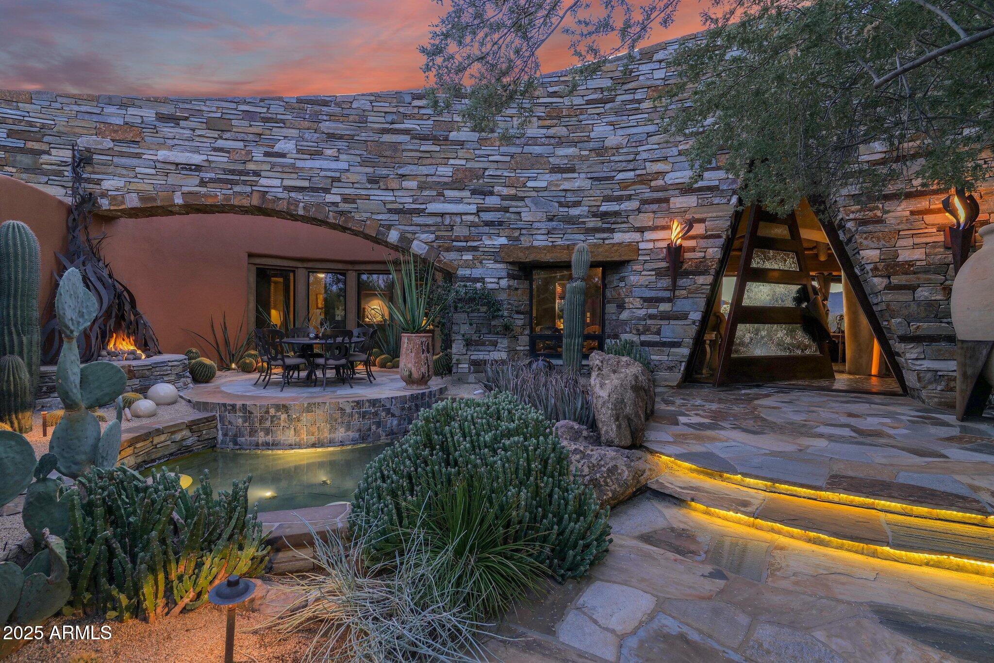 This stunning custom home, designed by renowned architect Shelby Wilson, is a masterful blend of stone, wood, and glass, harmonizing seamlessly with breathtaking desert surroundings. Set against a backdrop of rugged mountains and overlooking the pristine Boulders golf course, this architectural masterpiece embraces indoor-outdoor living with expansive glass walls that invite natural light and frame spectacular views. The main residence showcases warm wood accents, hand-selected stone finishes, and high-end custom details throughout. An open-concept design creates a seamless flow between the living, dining, and gourmet kitchen areas, perfect for both intimate gatherings and grand entertaining.

continue to more...... The primary suite is a private sanctuary with spa-like amenities, while additional bedrooms offer comfort and style. The "Moroccan Room" will be a delight for overnight guests, inviting peace and tranquility, private courtyard, scintillating fireplace.
Handsome den provides a sophisticated space for quiet conversation, floor to ceiling bookshelves invite you to unwind and dream.A luxurious guest house complements the property, featuring its own living space, two elegantly designed bedrooms, and premium finishes that reflect the main home's refined aesthetic.

Outdoors, a resort-style pool and spa provide a serene retreat, surrounded by thoughtfully landscaped desert flora that enhances the natural beauty of the setting. Tucked away is a charming potting shed, with copper sink beckoning any gardener to delight and create. This exceptional residence is a true testament to these original homeowners' visionary design where modern elegance meets organic materials, creating a timeless home in perfect harmony with its environment.