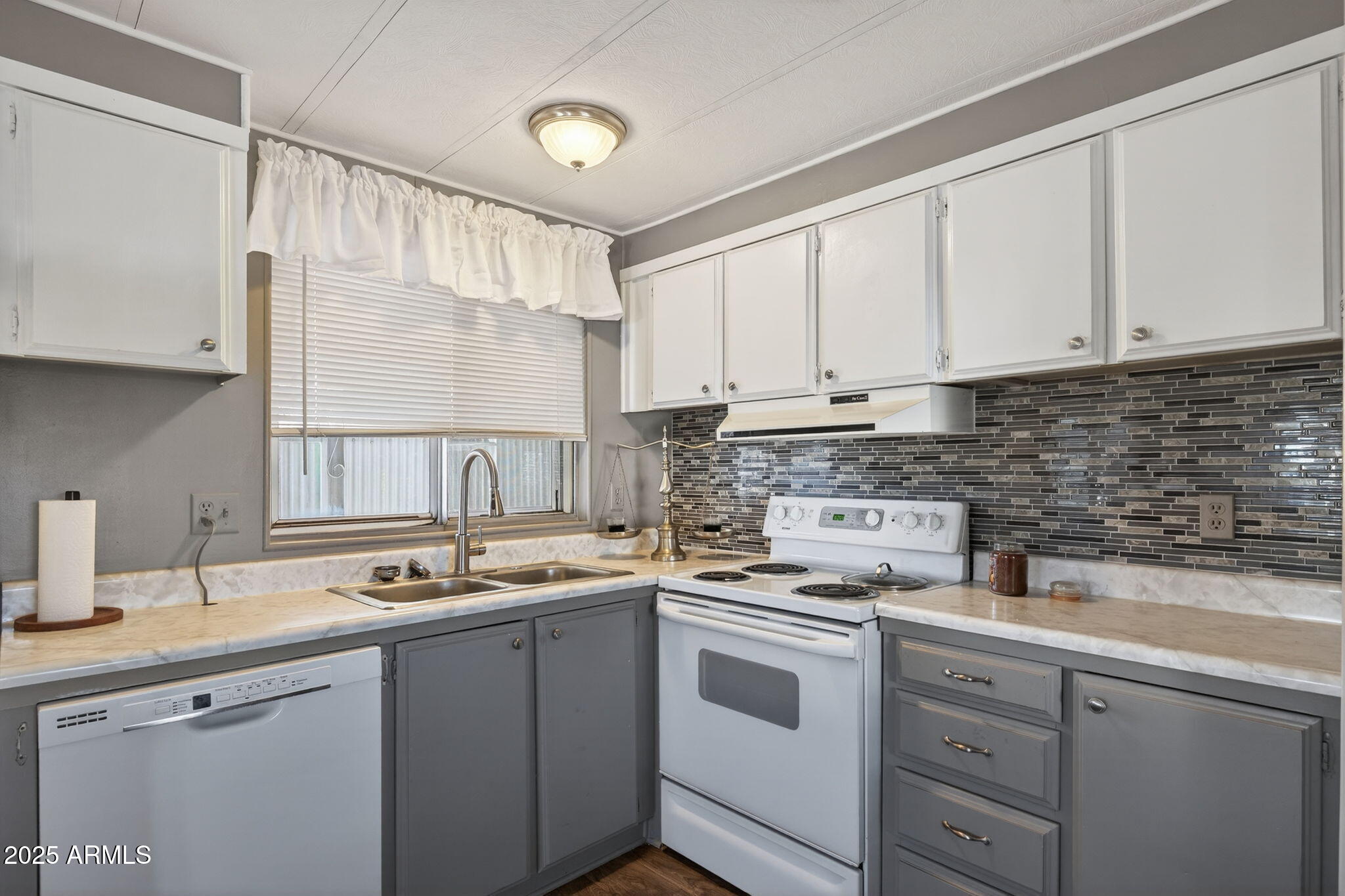 Not many like this come around at this price point. Single wide manufactured home in a well-kept community and it's ready to go. Two bedrooms, one bathroom, updated flooring, and neutral finishes. Refrigerator, washer, and dryer all convey, making it easy to settle right in.
The layout works well with open living flowing into the kitchen and dining area, generous cabinet space, a full appliance package, and built-in storage in both bedrooms. The extended vanity in the bathroom is a nice touch too. Out back you have a full-length covered patio with furniture that may stay, plus covered parking and a low-maintenance lot. The lot lease covers water, sewer, and trash keeping monthly expenses predictable. Central Mesa location with easy access to shopping, dining, and main roads. Sharp price. Fast close. See it before it's gone.
