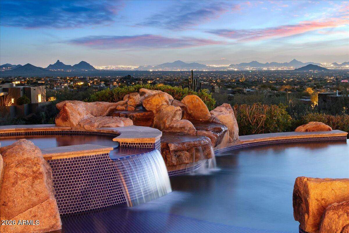 Stunning coastal California Style Retreat in Desert Mountain. Golf Membership Available. Experience the very best of Desert Mountain living in this beautifully maintained residence, perfectly positioned to capture dramatic panoramic views of the Valley of the Sun. Blending warm natural finishes with timeless architectural details, this exceptional home offers a seamless balance of comfort, elegance, and understated luxury. The light-filled great room serves as the heart of the home, showcasing beam-accented ceilings, a striking statement fireplace, and expansive windows that frame breathtaking desert vistas. Designed for both everyday living and effortless entertaining, the chef's kitchen features premium appliances, rich custom cabinetry, generous prep space, and an inviting layout. The spacious primary suite is a private sanctuary, offering serene views, a spa-inspired bath, with adjacent workout room and direct access to the outdoor living spaces. Thoughtfully separated guest suites ensure comfort and privacy for family and visitors alike. A standout feature of the property is the approximately 1,788-square-foot detached guest retreat, designed to elevate the hosting experience. This impressive space includes a private movie theatre, game room, family room a charming bunk room perfect for the grandkids, a convenient kitchenette, and an additional ensuite bedroom - creating an ideal setting for extended stays, multigenerational living, or unforgettable weekend gatherings. Step outside to a resort-style backyard designed to embrace Arizona's coveted indoor-outdoor lifestyle. Expansive covered patios, multiple seating areas, and a sparkling pool and spa create the perfect setting for sunset entertaining against the stunning desert backdrop. Located within the prestigious Desert Mountain Club community, residents enjoy access to world-class golf, dining, fitness, hiking, and an unparalleled lifestyle experience. Golf membership is available, offering a rare opportunity to become part of one of Scottsdale's most exclusive private club communities. This is Desert Mountain living at its finest -- where refined luxury meets effortless desert elegance.