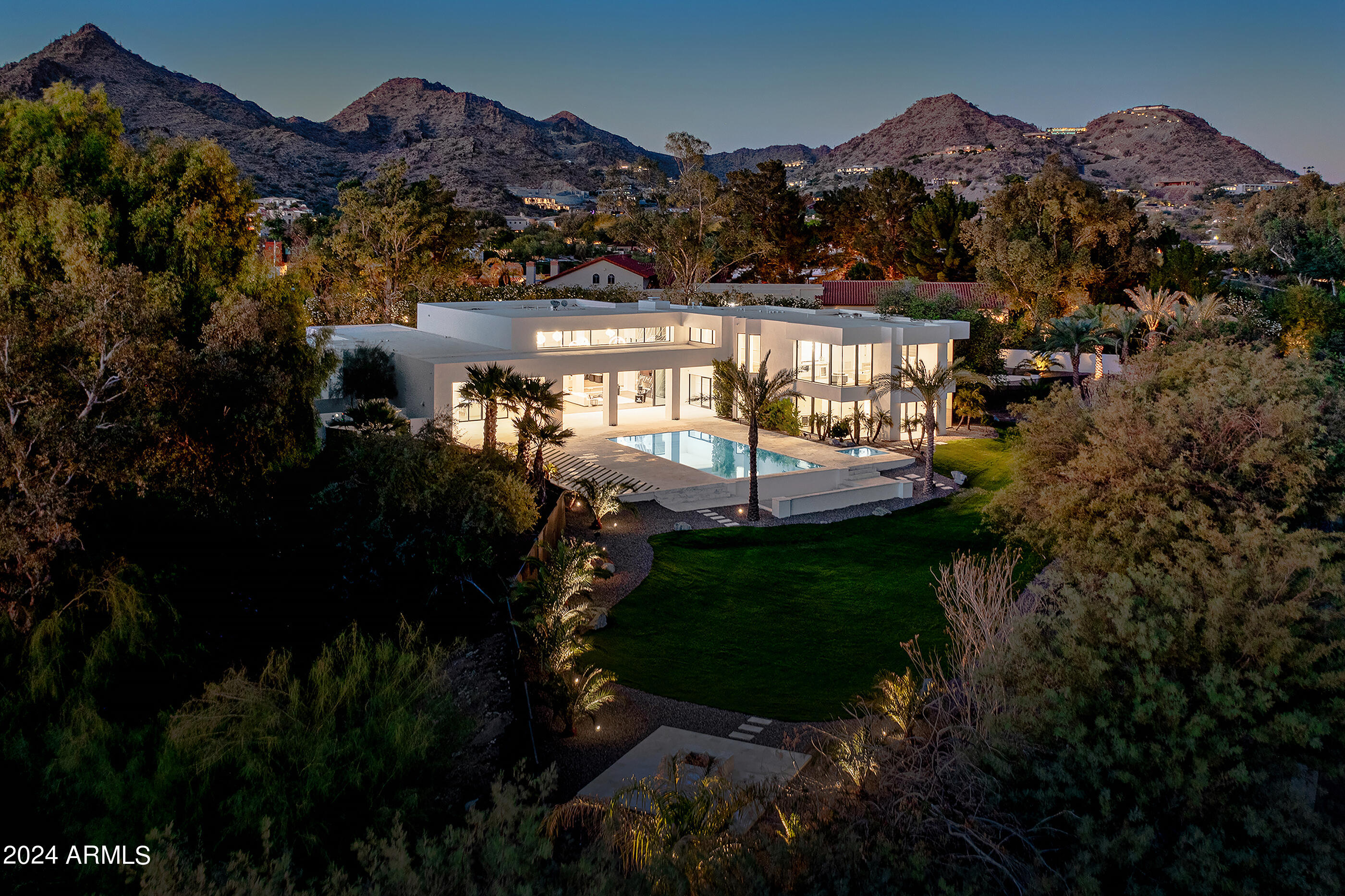 This glamorous estate is for those who appreciate artistic modern design coupled with classic elegance. Beyond the private gates sits a home loaded with sophistication and architectural excellence. The entry is accented by a copper clad pivot door that leads to exquisite living spaces. The kitchen features two twelve-foot islands, cabinetry imported from Spain, Wolf and Subzero appliances and a morning bar with built-in Miele coffee station. The entertaining areas are refined, yet comfortable and the flow of the home is flawless. The magnificent primary suite has floor to ceiling windows that frame views of Camelback Mountain spanning all the way to downtown Phoenix, and the primary bath will take your breath away. A 500-bottle wine room, 3-tiered movie theater, junior suite with an aromatherapy steam shower that would make a perfect home gym, wide plank oak floors with quartz inlays, marble and quartz accents, exceptional custom cabinetry, fully retractable walls of glass, custom ceilings, and opulent lighting are just a few of the exquisite design features inside, and the outdoor living is an absolute dream with a beautiful pool surrounded by sandblasted marble pavers, and a large yard with synthetic turf. The fully loaded Crestron home automation system includes lighting controls, security cameras and audio, both inside and out, and the driveway can accommodate up to 20 cars. This contemporary showpiece sits on 1.36 acres in a prominent Paradise Valley neighborhood!