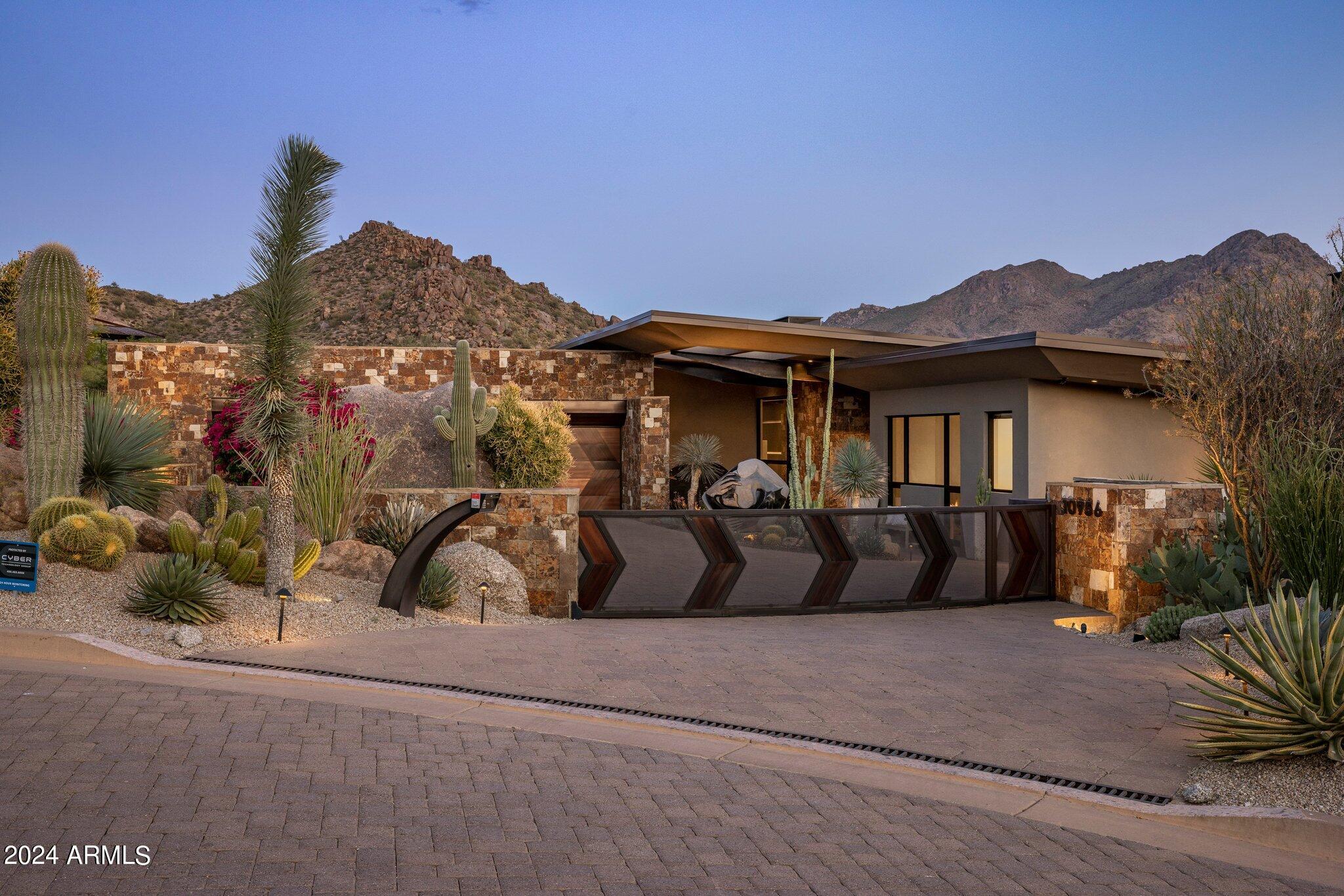 All about views! Enjoy living in the exclusive community of Tusayan at Troon. This contemporary timeless masterpiece exudes aesthetic simplicity, designed and built by renowned architect Mark Sever, is nested at the base of Troon Mountain, beautifully integrated in the natural site, framed with spectacular massive boulders. Completed in 2016, the masonry block construction is complemented by beautiful stone accent walls and striking metal roof lines. Gated community and privately gated, the property of almost an acre is professionally and extensively landscaped with a variety of mature plantings.
Enter the circular driveway including a covered parking for your guests, follow the paved walkway toward the circular stone water fixture to the artful glass front door opening  .. to 5300 sq ft of living space filled with natural light, great room with stunning stone open fireplace, 50 ft wide motorized pocket doors, creating an amazing indoor-outdoor entertaining space with spectacular panoramic views of mountains, city lights and the most gorgeous sunsets. High vaulted ceilings with steel beams throughout, open chef kitchen with large cooking island and sitting counter, generous walk-in pantry/back kitchen with sink and extra counter space for small appliances, built-in coffee maker, steam oven, attached cool room/wine room featuring a 332 bottles wine rack and additional cool food storage.
Master suite with expansive walk-in closet, fireplace opens to two private covered patios, north and south to enjoy the spectacular views of Troon Mountain and city lights. Two ensuite guest bedrooms, one with steam shower, and a very spacious office with fireplace and outdoor patio to contemplate Troon Mountain. 
The outdoor is a delight to enjoy the desert at its best and cool down in the 10 ft deep swimming pool, large covered patio for relaxation and entertainment, built-in grill and outdoor shower. Air conditioned 4 car garage. Golf membership options available, close access to outdoor activities, hiking, biking, golf, shopping and restaurants, and a few steps aways from the community pool and spa.
