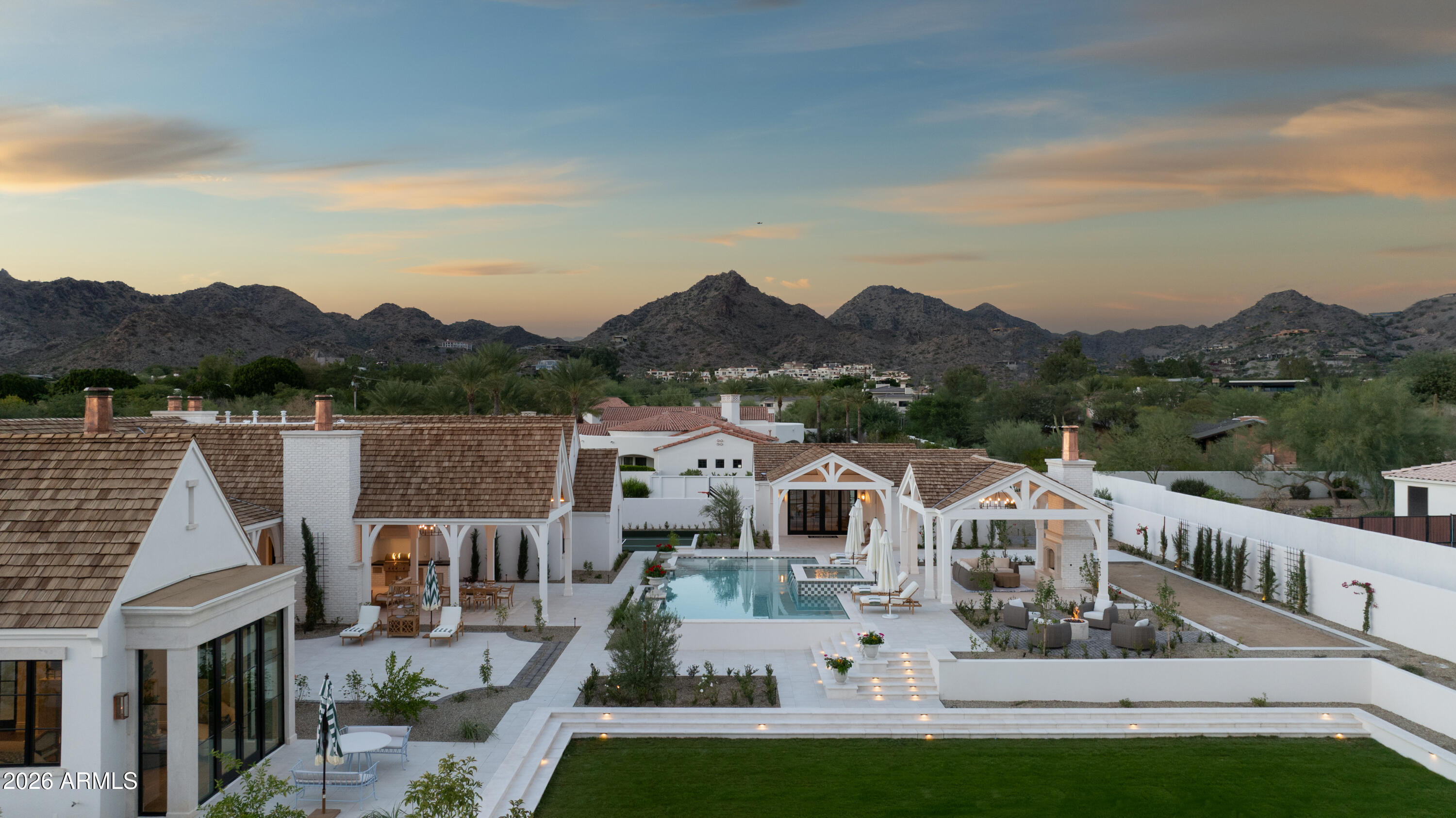Welcome to Maison de Vie, the 'House of Life,' set within the most sought-after neighborhood in Paradise Valley. Guided by a singular philosophy of 'One of One' blending transitional European design, art deco flair, and modern refinement that stands apart in a landscape of minimalist modern and old-world architecture.  Crafted through a seamless collaboration of artisans; the visionary Nate Gossage with Living Stone Builders, architect Jim Blochberger, interior designer Abby Kremer with George Oliver Design and Kristin Lane with Cedarhurst Home.  Their combined artistry and quality craftsmanship has delivered the most exquisite work of art.  
The exterior establishes an immediate sense of character with textured white brick, natural limestone detailing, copper chimney caps, and a... cedar shake roof rising into sweeping rooflines that hint at the grandeur within.  A gated stone path leads to the dramatic entry, where a black-lacquered custom front door opens into a foyer layered with intricate millwork and stonework. The great room unfolds with a wall of pocketing glass sliders that invite natural light across the limestone-clad fireplace and warm, intentional finishes. Every selection throughout the home draws from transitional European influence, art deco richness, and modern restraint, resulting in a residence that feels both timeless and deeply livable.
At the heart of the home, the gourmet kitchen is a centerpiece of function and beauty. Dual marble-topped islands anchor the space alongside SubZero and Wolf appliances, a sculpted plaster hood, and pocketing pass-through windows that blur the line between interior and exterior living. A fully appointed service kitchen elevates both everyday efficiency and hosting capacity, offering additional SubZero refrigeration, marble prep surfaces, and exceptional storage for seamless entertaining. The formal dining room is conceived as an immersive environment of color and craft. A custom coffered ceiling cascades down the walls with sculptural precision, complemented by crystal lighting, a 144-bottle wine wall, and a limestone fireplace creating an immersive dining experience.
The primary suite is a private sanctuary shaped by softness, warmth, and restorative calm.  A limestone fireplace grounds the room, while wood-beam ceiling details create a sense of architectural intimacy.  French doors open to an outdoor patio, allowing landscape and architecture to merge.  The spa-inspired bathroom continues the retreat-like experience, opening to a secluded patio and tranquil courtyard garden, an ideal setting for morning quiet or evening reflection. Marble tiled walls, a lighted niche within the shower, and dual vanities offer both beauty and function. A dedicated coffee station with Wolf coffee maker and refrigerator drawers completes the suite; curated for ritual, rest, and elevated daily living.
Designed for comfort and privacy, the guest wing offers its own enclave within the home.  A media room anchors the space, opening to a covered patio that extends the functionality of the wing outdoors. Three ensuite bedrooms are placed with thoughtful separation, each offering a calm, indulgent environment consistent with the home's broader aesthetic. The mood throughout is one of considered refinement, allowing guests to settle effortlessly into their own retreat.
Just beyond the central living space, the home reveals a whimsical pantry and a moody utility room, each space crafted with charm and intention. The pantry feels almost storybook in its detailing, transforming organization into an artful experience.  In contrast, the utility room introduces deeper hues and a sculptural sense of order with floor-to-ceiling cabinetry, a central work island, and a full Electrolux laundry system.  The adjoining mud room features an integrated pet-feeding station built seamlessly into the millwork, a thoughtful nod to the four-legged family members of the home.
The Arizona outdoors become a natural extension of the estate through a sequence of meticulously composed living spaces. Expansive covered patios transition to a ramada framed by handcrafted timber beams and defined by a limestone fireplace, establishing a serene backdrop for gatherings.  Multiple seating vignettes are positioned to capture views of the manicured lawn and the desert horizon. As evening approaches, elevated LED-lit steps guide you to the upper ramada where the negative edge pool and spa unfold, complete with a cascading water feature that adds movement, light, and sound to the landscape. This elevated terrace becomes an open air lounge, an intimate perch overlooking the water and mountains.
A private pathway extends beyond the pool to the detached guest house, offering visitors their own complete residence with a living area, kitchen, and bedroom. For recreation, a dedicated sport court invites play and activity, rounding out the estate with a thoughtful balance of energy and tranquility.
Every moment of this home indoors and out, has been shaped with craftsmanship, intention, and artistry.  Maison de Vie is more than a residence; it is a composition of architecture, material, and emotion created for those who appreciate design at its highest expression.