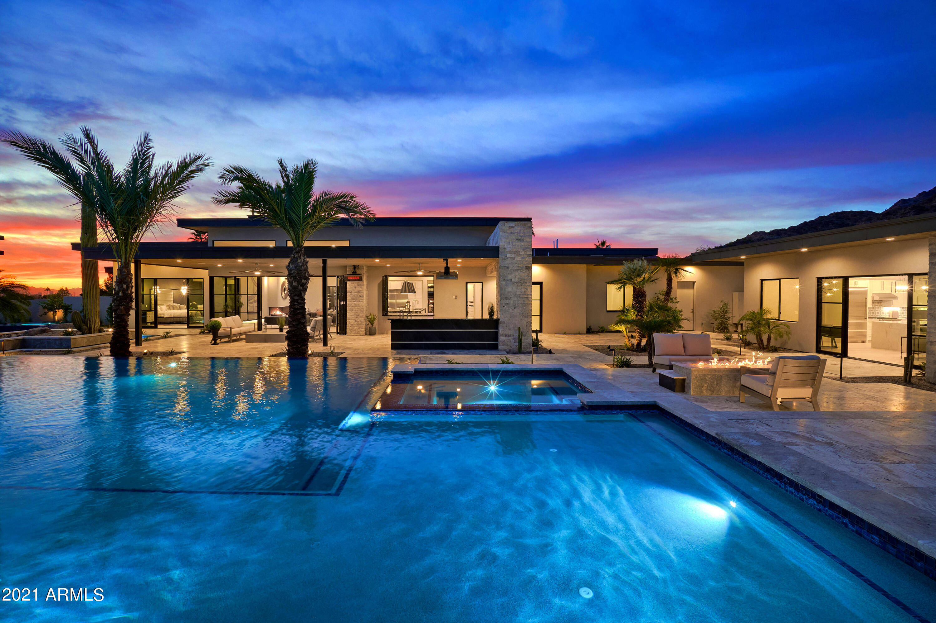 This stunning, contemporary Paradise Valley estate is everything you're looking for in modern design, backed by unparalleled craftsmanship. It's a centrally-located urban masterpiece that boasts exterior accents of split-faced silver travertine stone, and tongue & groove wood eaves surrounded by soaring palm trees with spectacular mountain and city light views. The main home has a thoughtfully-designed split floorplan, allowing for privacy from the guest suites. Home features European White Oak wide plank wood flooring throughout, 5 spacious suites, 2 powder bathrooms, a large chef's kitchen with solid shaker-style cabinets (including soft-close full extension drawers and soft-close doors),  (See supplement) Sub Zero, Wolf and Cove appliances, 7-foot galley kitchen sink, large main pantry and butler's pantry with full kitchen.
Kitchen amenities include a large island draped in Belvedere quartzite with built-in tv lift. And the pass-through window from the main kitchen to the full outdoor kitchen makes entertaining any size group seamless.
Your open concept great room features a cozy linear fireplace, cooled double-faced glass wine wall and full bar. The formal dining room opens to a paved courtyard with water feature and outdoor fireplace. Then, retreat into your luxurious master suite featuring a linear fireplace, beverage station and large Western slider providing walk-out access to the backyard where a private master spa awaits. The spa-inspired master bathroom includes spacious his-and-hers closets, his-and-hers toilet rooms, stacked laundry, luxurious shower, and separate, freestanding pedestal tub.
Secondary ensuites feature a separate living area/game room across from the theater room. Guests will enjoy the detached guest house built with the same quality as the main home including 1 bedroom, 1 bathroom, full kitchen, great room area and laundry room.
The home's circular driveway provides access to an attached 4-car garage with built-in cabinetry, water filtration system, Rinnai tankless hot water system, epoxy flooring and attached RV/boat garage with a 12-foot garage door and 38 Ft deep.
This home brings the resort to you: The luxury backyard features a huge, covered tongue & groove patio with full outdoor kitchen, commercial mister system, gas Bromic platinum smart heaters, sparkling negative edge pebble tech pool, large format travertine pool decking, Baja shelf, swim up bar, sunken area and fire features. In this one-of-a-kind luxury estate, immaculate construction meets the ultimate in style and design.