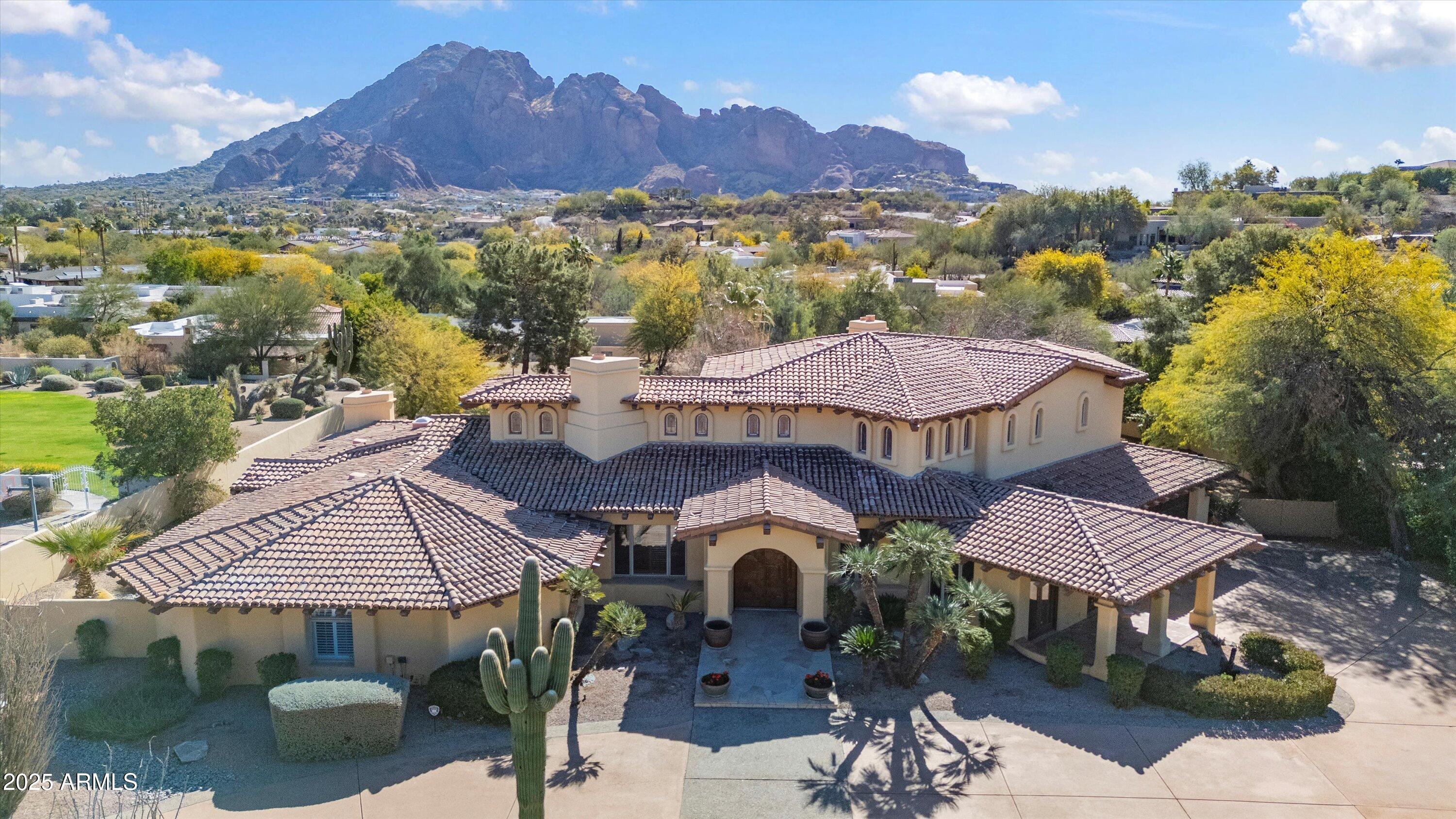 Located in the exclusive, gated community of Clearview Edition, this 1-acre Spanish Revival estate offers unparalleled privacy and enviable Camelback Mountain views. Step into an expansive floor plan featuring soaring ceilings, exposed wood beams, and hand-painted Mexican tile accents that exude warmth and charm. Every inch of the 6456 sq. ft. home was thoughtfully designed. The living room with two-way fireplace, wet bar, and soaring arched windows has a wall of center-glassed doors to connect to the stunning resort backyard. Off the well-appointed kitchen, the formal dining room with a beamed ceiling and dramatic iron chandelier is perfectly sized for your dinner parties. The primary suite on the 2nd level offers a private sanctuary with a spacious bedroom, sitting room, and 2 walk-in closets. A private view deck from the suite provides a serene retreat to enjoy morning coffee or evening sunsets. Four guest bedrooms are located on the east wing. The outdoor living spaces are equally impressive, offering a true resort-style experience. A pool and spa invite relaxation, while the poolside ramada provides a shaded retreat. Sports enthusiasts will appreciate the sport court and putting green.  Beyond its undeniable beauty, this estate enjoys an enviable location with easy access to shopping, fine dining, golf courses, and Sky Harbor Airport, making travel and leisure convenient.