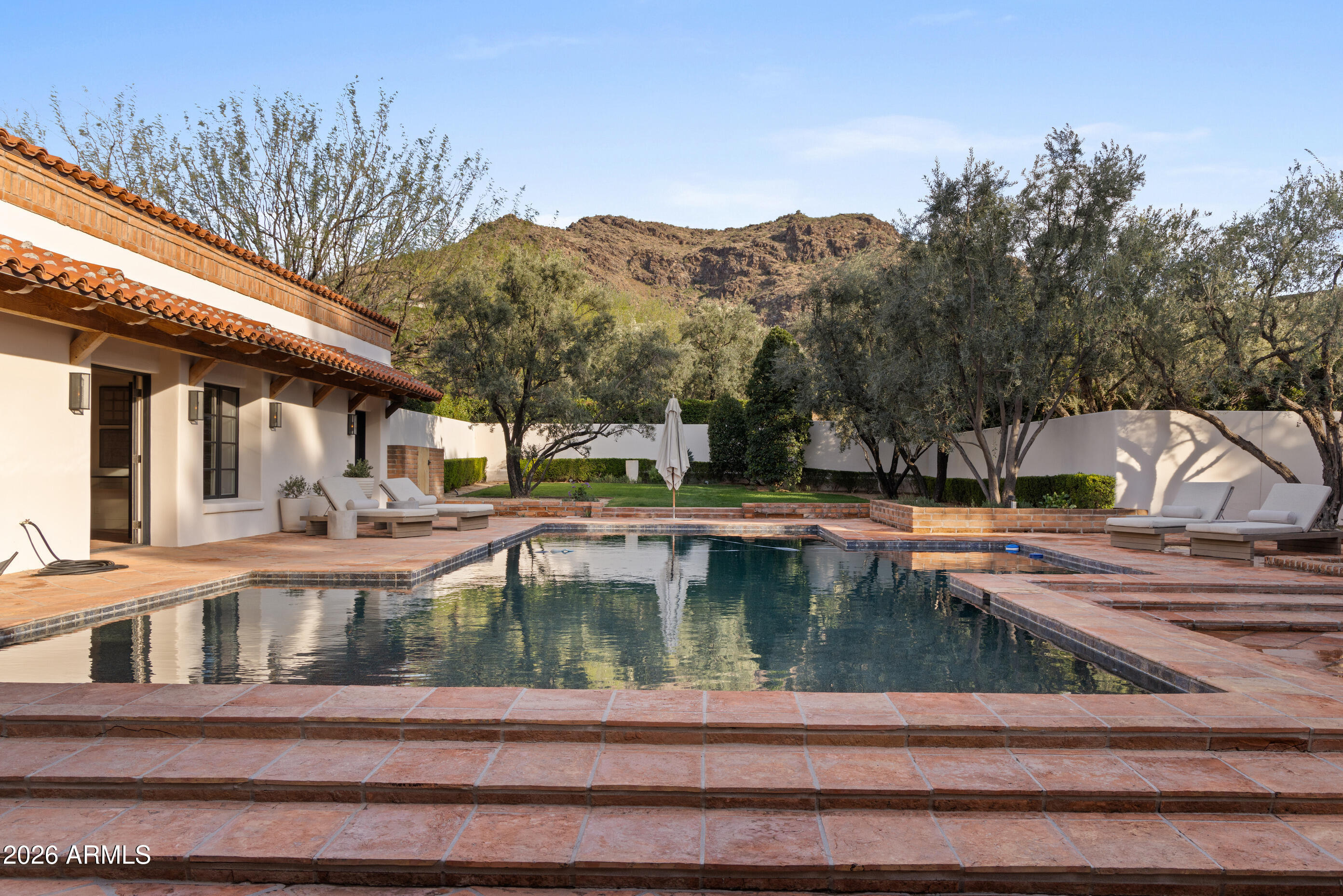 A rare offering on the 4th fairway of Paradise Valley Country Club, this 6604 sf desert/modern - extensively remodeled (GM Hunt 2013) estate blends timeless character with a refined modern edge. Highlighting a private courtyard pool, the home features Saltillo and wood floors, floating beam ceilings, and restored antique doors. Framed by views of Mummy Mountain in the front and the Phx Mountain Preserve beyond, the home sits along the golf course, offering a picturesque setting. The backyard is designed for both entertaining and everyday living, w/multiple patio spaces, expansive lawn, mature trees, and a curated vegetable garden. The primary suite features vaulted ceilings, a spacious bathroom, 2 water closets and large dressing room. The reimagined kitchen showcases mid-century modern... influence with Viking appliances, double ovens, a prep kitchen, and ample storage. Multiple living areas open seamlessly to lush grounds with olive and citrus trees, grass, and a brick patio w/ firepit. Three additional bedrooms, an office/library, 4 car garages + flexible spaces offer versatility. A warm, architecturally rich property in one of Paradise Valley's most coveted locations.