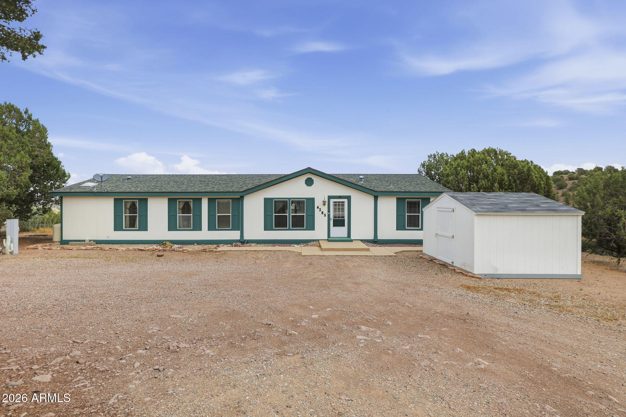 Wide-open Chino Valley views, room to breathe, and peaceful country living. Welcome to 6285 N Gray Gos in Chino Valley, AZ, a spacious manufactured home on a fenced property with sweeping mountain and valley views, mature trees, usable outdoor space, and a storage shed. Inside, enjoy warm wood-look flooring, a cozy living room with stone fireplace and built-ins, large view-filled windows, and a kitchen with abundant cabinetry, tile flooring, gas range, skylight, and generous counter space. The primary suite offers dual sinks and a soaking tub, while additional bedrooms add flexibility for guests, office, or hobbies. Relax on the covered deck and take in the quiet Arizona scenery.