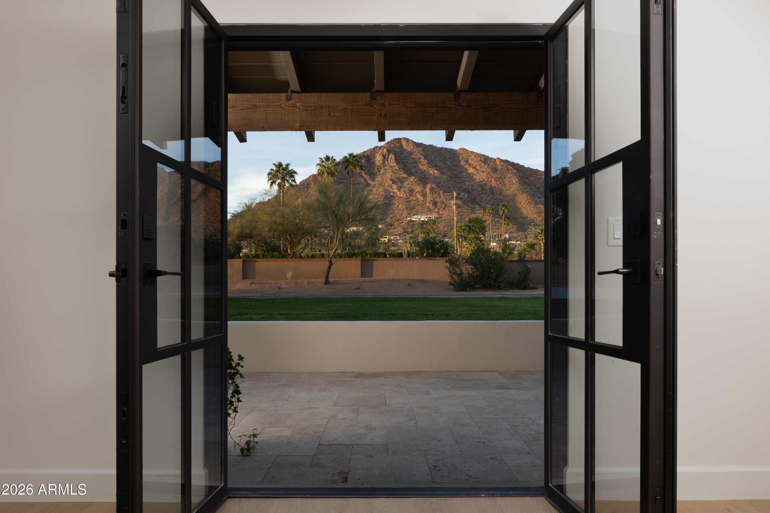 Set on a private, lush drive off Camelback Rd sits a refined interpretation of Spanish Colonial architecture. This residence blends authentic old-world materials with a calm, contemporary sensibility. Set on a .77-acre lot with striking Camelback Mountain views, the home pairs warm minimal interiors with globally sourced artisan details, creating an atmosphere of quiet, textural luxury. The custom kitchen is both sculptural and functional, featuring bespoke cabinetry with unlacquered brass hardware, an oak-stained island with farm sink and bridge faucet, and paneled Fisher & Paykel refrigeration and dishwasher. A statement ILVE range anchors marble countertops in Calacatta Gold with ogee edge and full slab backsplash. Antique doors introduce patina and character, while an adjacent butler's pantry offers white oak shelving, wood countertops, wine refrigeration, and abundant storage. Hand-applied Roman clay walls and surrounds enrich the range hood, fireplace, and all baths, complemented by custom Murano sconces and handmade solid brass lighting throughout. White oak flooring flows through serene living spaces softened by linen draperies and framed by custom iron doors and additional antique architectural elements. The generous primary suite is a private retreat with soaking tub, dual custom white oak vanities, antique mirrors with hand-forged brass frames, Turkish limestone floors, and a Zellige tile shower enveloped in Roman clay walls. Secondary baths continue the material story with Spanish ceramic tile, Calacatta marble mosaics, solid unlacquered brass plumbing, and an antique marble-topped vanity. The powder bath is wrapped in dramatic Breccia Capraia marble.

Outdoors, Saltillo-tiled patios overlook refreshed pool finishes with Zellige waterline tile and mini-pebble interior, all set within expansive grounds oriented to Camelback views. A travertine-paved entry courtyard with limestone trough fountain completes the home's layered Mediterranean narrative.

Timeless Spanish roots, Moorish influence, and warm minimal restraint converge in a residence that feels both historic and distinctly modern.