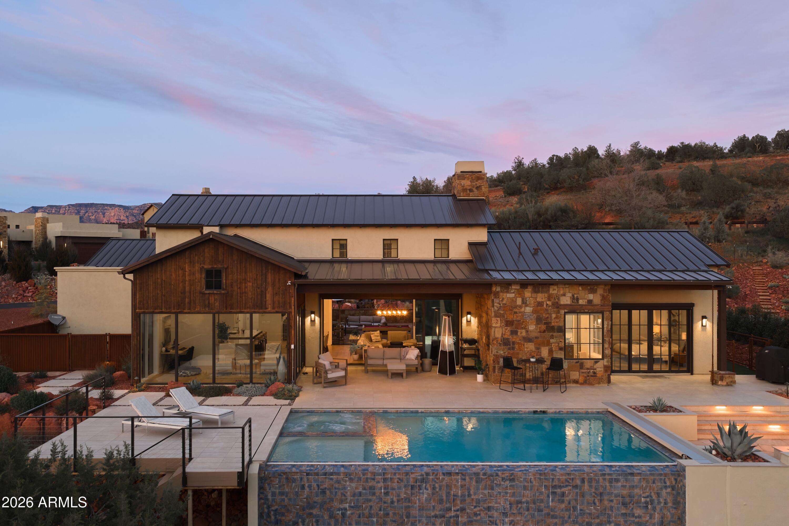 ELEVATED LIVING within the gated community of Sedona Ranch on Oak Creek, this 2,928 sq ft modern ranch-style home offers 3 bedrooms, glass bonus room, and seamless indoor-outdoor living framed by sweeping red rock views. Vaulted ceilings and a dramatic floor-to-ceiling stone fireplace anchor the light-filled great room, flowing into a chef's kitchen with rich custom cabinetry, premium appliances, and an expansive stone island. Walls of glass open to a resort-style backyard featuring a negative-edge pool, firepit lounge, and panoramic vistas across Oak Creek toward Mingus Mountain. A private front courtyard creates an intimate gathering space, complemented by a charming cantina window for effortless entertaining. Enjoy dual private road access to both Sedona and the Village of Oak Creek.