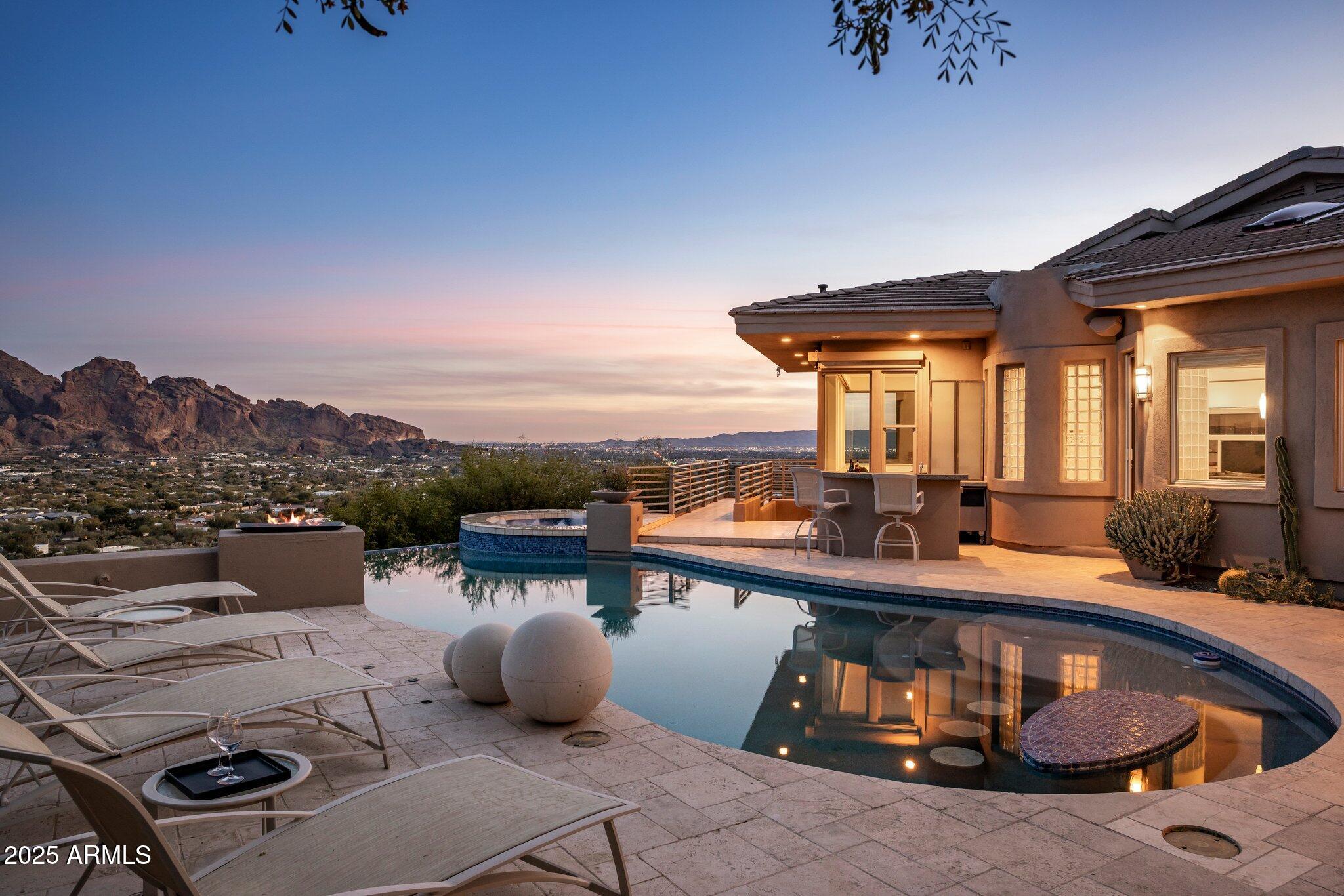 Celebrated in prestigious publications like Phoenix Home and Garden and Sunset Magazine, this architecturally distinctive premium view property is a true masterpiece that must be experienced to be fully appreciated. Perched atop its own private peak, this elite residence combines unrivaled views, architectural artistry, and engineering excellence in a way that is both breathtaking and unforgettable.
Spanning a total of 5,394 SF on an elevated acre lot, this residence offers panoramic views that stretch across Paradise Valley, Scottsdale, and out to the majestic Four Peaks and Superstition Mountains. It features a 3-bedroom, 3.5-bathroom main house and a detached 1-bedroom, 1-bathroom guest house with its own private entrance, perfect for guests, multigenerational living, an income property or even as an executive retreat.
From the moment you arrive, you'll be captivated by a dramatic 40-foot waterfall carved into the mountainside, setting the tone for what lies ahead. Inside, the open-concept design blends soaring ceilings, floor-to-ceiling glass walls, and architectural creativity to integrate the indoors with the stunning surrounding landscape.
Unlike the typical modern designs flooding the market, this elegant organic modern home sets itself apart with its soft curves, earthy tones, and striking architectural features.
The gourmet kitchen has Viking and Sub-Zero stainless steel appliances, a built-in Miele espresso machine, and Poggenpohl cabinetry with fronts of warm wood, glass and stainless steel. This is paired with sleek, diagonally cut granite countertops. A striking cone-shaped stainless steel hood and a hidden pantry tucked behind  glass doors add to the space's allure. The bold, triangular granite bar in the living room serves as a sculptural centerpiece, perfectly positioned for intimate evenings or grand events that have included 450 guests. One such event included an aerialist circus act that performed over the pool on engineered trussing. (See Documents tab for published articles).
The primary suite is a private sanctuary offering sweeping views that command your attention, a spacious lounge, and a boutique-style closet with locking mullion cabinetry and custom jewelry inserts.The spa-inspired master bath brings resort-level luxury, boasting granite trough sinks and a customizable shower equipped with a temperature dial, rainfall feature, body jets, and a handheld spray. The guest house captures panoramic mountain views and offers an unparalleled level of comfort and privacy with its own entrance, lounge area, bath and private patio.
Step outside, and the magic continues. A two-story, wraparound patio features five distinct seating areas. Nearby, there is an outdoor kitchen, a resort-style full bar with seating and the centerpiece of the space: a spectacular negative-edge pool and spa. Perched at the edge of the hillside, this dramatic space highlights the elements of fire, water, and stone, creating an atmosphere that feels as though you're floating on air.
The lower level of the home offers a versatile space for entertainment or work, with floor-to-ceiling windows, a state-of-the-art retractable movie screen, projector, and sound system. This level also features an exercise area, two executive offices or guest rooms,  a sleeping area with a Murphy bed and spa-inspired ensuite bath with a trough sink, rain shower and floating toilet.
Designed for lock and leave convenience, the property features low-maintenance native landscaping, turf, and a fully automated electric and audio-visual system.
This entertainer's paradise is a living work of art. From the stunning architecture to the jaw-dropping views, this is a home that you will admire every time you step inside. You simply have to see it to believe it.