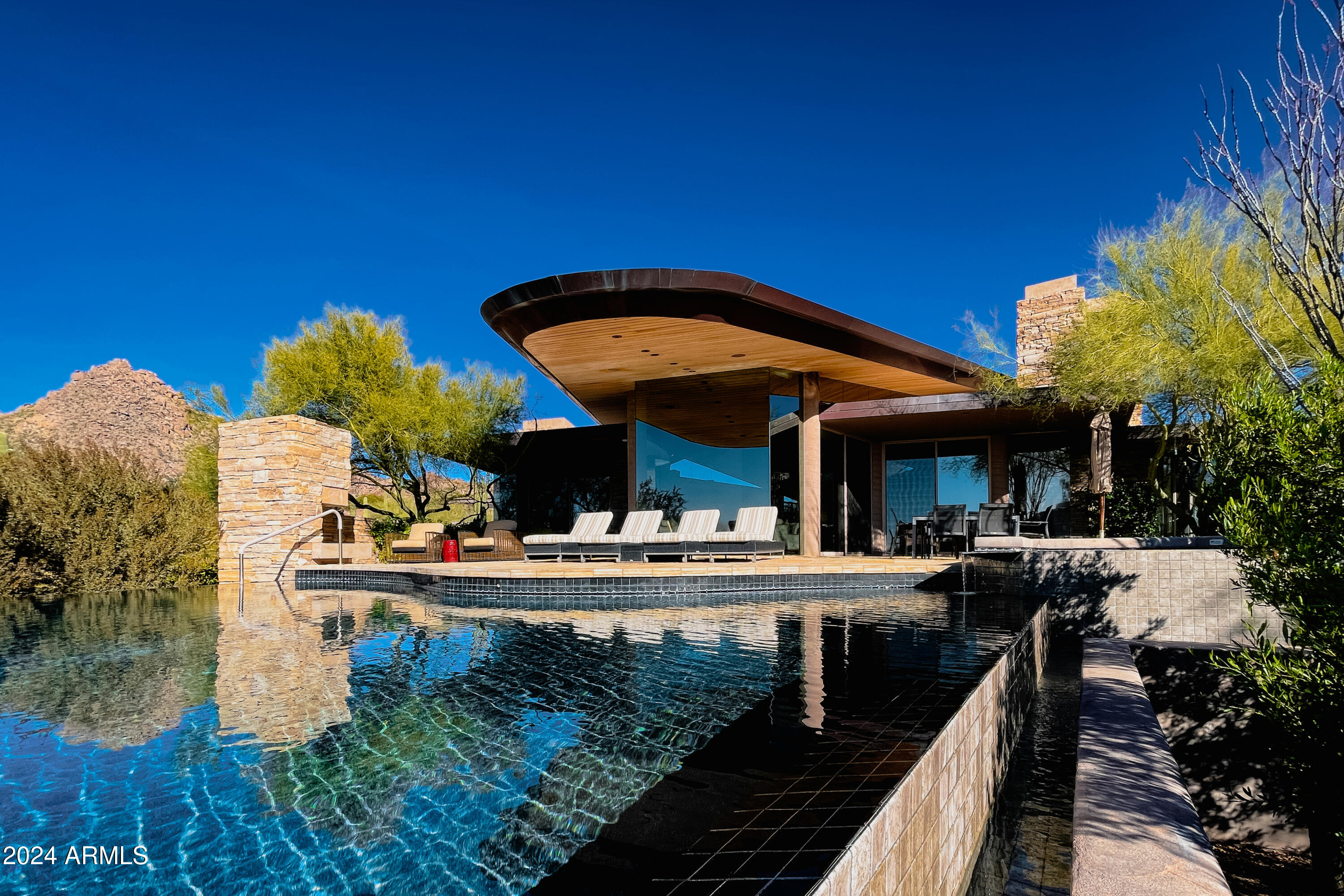 This home is an architectural gem with a truly timeless feel, on the market for the first time since winning the Arizona Home of the Year / Honor Award in 2001. Designed by the renowned architect Gordon Rogers, this estate embodies the best of organic contemporary architecture. This is a rare opportunity to own a masterpiece in the exclusive, guard-gated community of Glenn Moor at Troon Village. Known for creating homes that merge seamlessly with their natural surroundings, Rogers' vision is evident throughout this property, which has been thoughtfully updated by its current owners while preserving its original design integrity. The estate's layout is divided by a natural arroyo, which created the perfect design opportunity to connect the guest house on one side with the main... residence on the other, for an organic flow. The dramatic approach takes guests up broad concrete steps and across a bridge, culminating in a striking 9-foot-wide pivoting entry doora bold first impression.

The main house offers 6,030 square feet of meticulously crafted living space, with an additional 1,030 square feet in the detached guest house, bringing the total to 7,060 square feet. Inside, the great room stuns with a soaring ceiling with beautiful tongue and groove wood, supported by four concrete columns and two sculptural steel fins, and is framed by high clerestory glass walls that capture panoramic views of the surrounding mountains.

The floating roof, with its cantilevered ends, mirrors the curves of the land and the infinity-edge pool, both of which reflect the natural topography. Hand selected from the quarry, the Utah sandstone found throughout the home blends harmoniously with the desert landscape. The same stone is used for both walls and floors, creating a seamless flow from the interior to the outdoor spaces.

A real once-in-a-lifetime estate that truly encompasses architectural feats known only to select residences. Offering a perfect blend of cutting-edge architecture, natural beauty, and modern upgrades, this home is designed for the discerning buyer seeking a uniqueness rarely made available.

Most furnishings and accessories available by separate bill of sale.