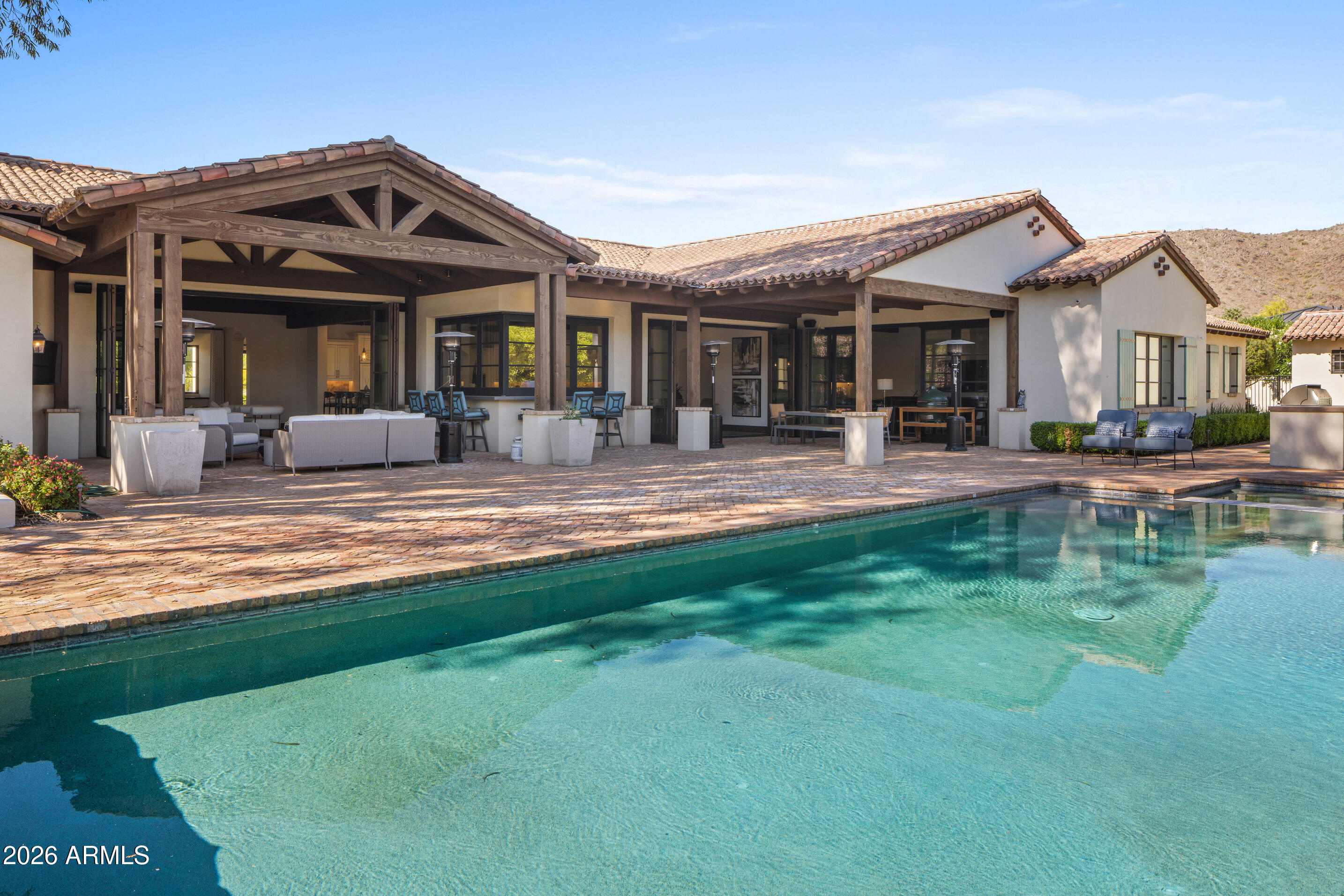Set on a quiet, highly desirable street near Paradise Valley Country Club, this beautifully designed home spans 7,703 sqft and offers lovely views of Mummy Mountain, Camelback Mountain, and the surrounding preserve. The 5-bedroom main residence is complemented by a private detached guest house--ideal for visitors or a dedicated office. Designed for effortless indoor/outdoor living, a full bar w/ retracting windows opens to an expansive covered patio w/ TV lounge, dining area, & a lap pool positioned to take in the mountain backdrop. The grounds feature a putting green, bocce court, lush grassy areas, & mature trees. Inside, warm farmhouse elements--wood-beamed ceilings, Chicago brick, & wide-plank floors--frame a spacious chef's kitchen with large island & breakfast room, along with.... a formal dining room with a brick-inlaid ceiling and adjoining wine room. A split floor plan offers a private primary retreat with patio, coffee bar, and spa-like bath, plus an oversized game room and additional ensuite bedrooms. A rare blend of scale, character, and livability in one of Paradise Valley's most coveted locations.