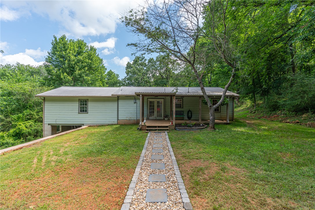 The work has already been done for you,the chicken coop is built and the garden is planted! Discover this charming 1,744 sq. ft home nestled on 2.49 acres in beautiful Mountainburg, walking distance from the school. Beyond the features you can see, the owners have invested in valuable improvements, including a large retaining wall, buried electrical service to the garage, and a rock-lined drainage ditch to help manage runoff.Inside, you'll find 3 bedrooms, 1.5 bathrooms, a spacious eat-in kitchen, and a newly installed coffee bar.  Grab your coffee and relax in the heated and cooled sunroom, the perfect place to start your day while taking in the peaceful surroundings. The oversized living room offers incredible flexibility and is currently arranged with both a dining area and office space, making it easy to adapt to your lifestyle. A welcoming covered front porch provides the perfect spot to unwind. If you've been dreaming of country living with room to grow, come take a look at this special Mountainburg property!