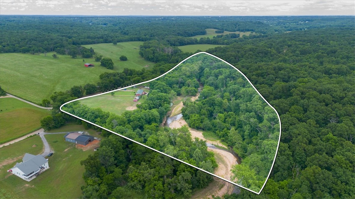 One of a kind creekfront retreat on Little Spavinaw! This private, park-like property features the creek running through the land, a natural spring, wooded acreage, horse pasture, trails, and a cave across the creek. Flat, usable land and peaceful surroundings make this a truly special property you’ll want to keep in the family for generations to come. The creek is steps away from the lovely home that includes a huge kitchen with island, undercabinet lighting, and two dining spaces. Large primary suite with all the modern amenities. In ground saltwater pool and pavilion, storm shelter, and multiple outbuildings including a charming 15x12 Creekside cabin with a large 19x16 deck overlooking the water — perfect for an office, craft room, guest bunkhouse, or relaxing getaway space.