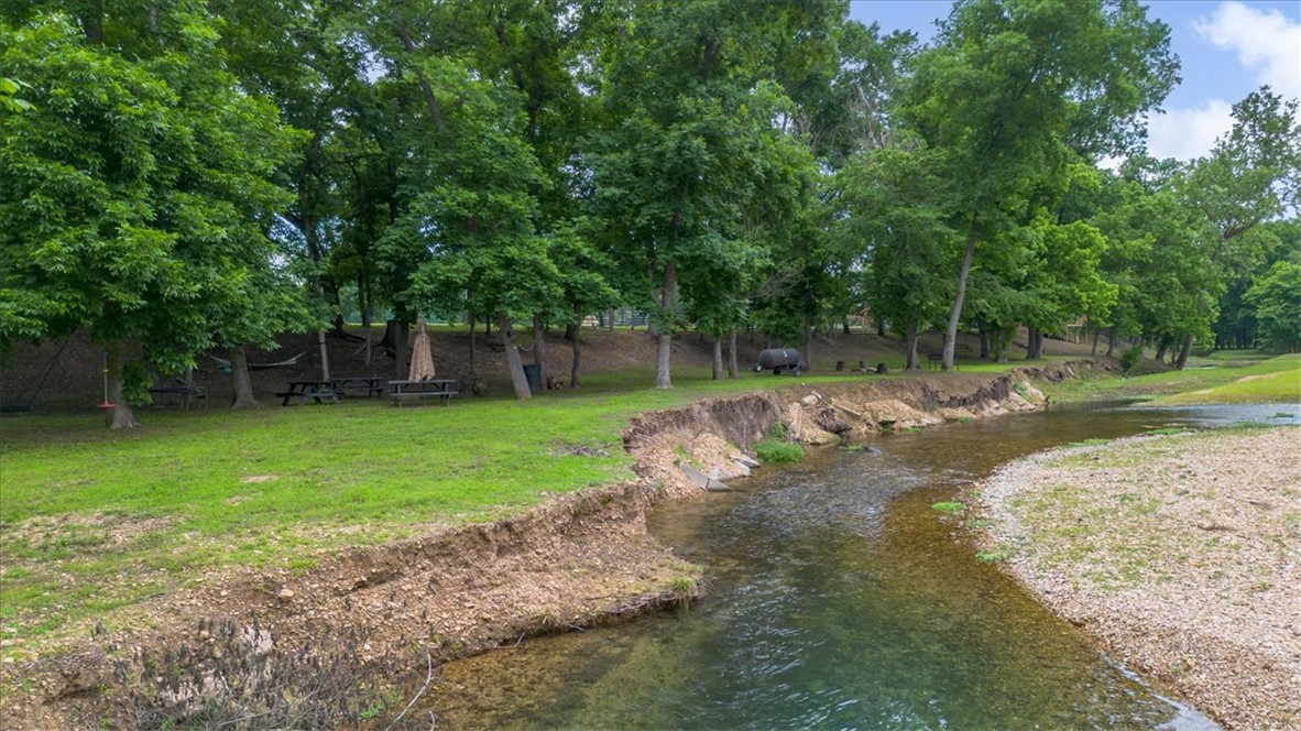 One of a kind creekfront retreat on Little Spavinaw! This private, park-like property features the creek running through the land, a natural spring, wooded acreage, horse pasture, trails, and a cave across the creek. Flat, usable land and peaceful surroundings make this a truly special property you’ll want to keep in the family for generations to come. The creek is steps away from the lovely home that includes a huge kitchen with island, undercabinet lighting, and two dining spaces. Large primary suite with all the modern amenities. In ground saltwater pool and pavilion, storm shelter, and multiple outbuildings including a charming 15x12 Creekside cabin with a large 19x16 deck overlooking the water — perfect for an office, craft room, guest bunkhouse, or relaxing getaway space.