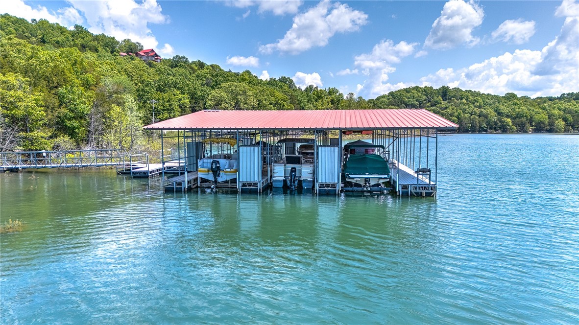Stunning wooded lakefront property on Beaver Lake with incredible views and thoughtful amenities! This home includes a covered boat slip with a solar powered electric lift plus a ½ slip for a jet ski (uncovered). Floor-to-ceiling windows in the main living room offer breathtaking lake views and allowing natural light to pour in. A gorgeous wood ceiling, original Vermont Castings wood stove, and custom built-ins create a cozy space. The primary bedroom, conveniently located on the main floor, has an en suite bath featuring a walk-in shower. Enjoy a four-season sunroom that opens to a wraparound deck. The walk-out lower level offers a second living area complete with a snooker table and a safe room. Adjacent to the garage is a rock patio for additional outdoor space. The lower-level screened-in porch is plumbed for a hot tub. For parking and storage, there’s a 3-car garage (2 attached, 1 detached) plus an RV parking pad—plenty of room for all your vehicles and toys. There is a whole house generator for peace of mind.