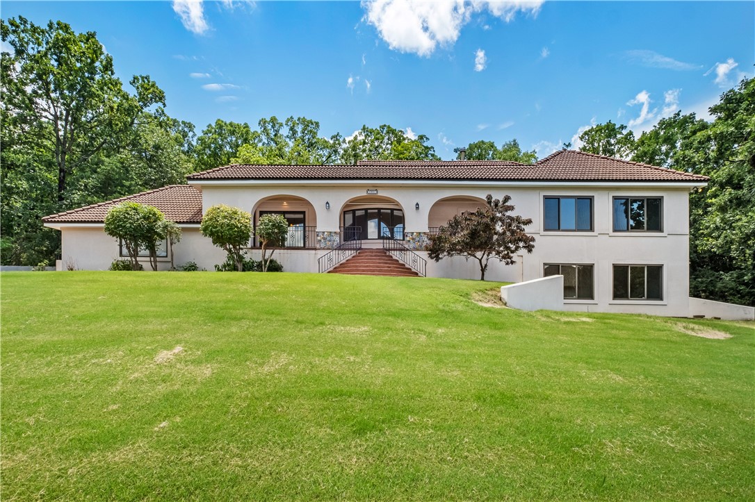 Welcome to Oaks Manor, where Spanish Revival charm meets modern comfort. This unique and stately hilltop home sits on a private half-acre in Fayetteville’s desirable East Side. Oaks Manor exudes warmth and character with 3 outdoor patios, 2 fireplaces, and a custom wood spiral staircase. The main level features 2 spacious living areas plus 3 bedrooms, including a cozy, light-filled primary suite with patio access. The kitchen features recently remodeled quartz countertops adjacent to formal indoor and outdoor dining areas and living room. Downstairs, you’ll find 2 bedrooms, full bath, game rooms with pool table, a library with built-ins and wet bar. Discreet Invisible Fencing allows pets to roam freely while remaining safely on the lush, green property. Friendly deer, rabbits and the occasional owl come visit. Includes a 2-car garage and is close to parks, shopping, dining —plus quick access to I-49. Ideal for entertaining and hosting out-of-town visitors. It’s a magical home for families of all types and ages.