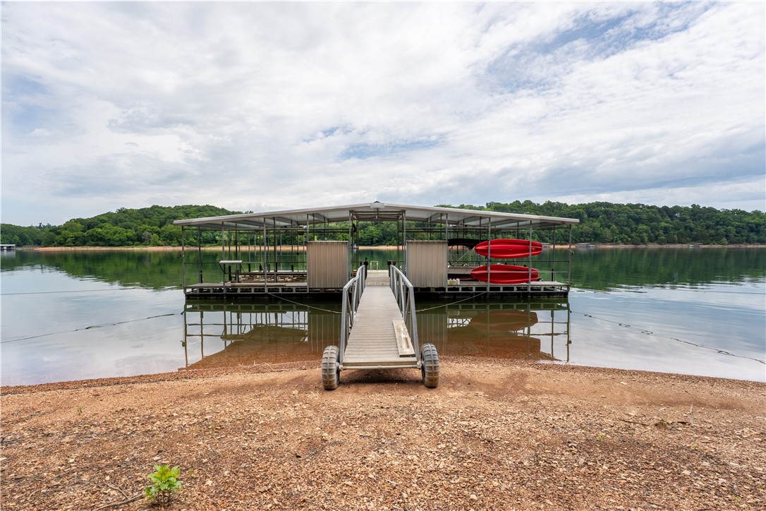 Back on market due to no fault of sellers. Beautiful lakefront home offers everything you would expect from a designer lake home oasis. Entering the home you're impressed w/high-end finishes & natural light. There is 2 family living areas, 2 fireplaces w/heatilators & a bonus room. Kitchen has a large island w/sitting for 6, separate coffee bar & walk in pantry. Enter the spacious primary suite on the main level thru 2 glass french doors. This home offers a whole house fan. Safe room located under the stairwell. Cedar closet & solid maple cabinets in the utility room. Patio has stamped concrete flooring, 1 deck has porcelain tile flooring, 2nd deck has tiger wood flooring. Home has hand-scraped hickory flooring. .91 acre of a manicured lawn, RV storage w/30 amp electric service, 3 car garage w/workshop & 2nd workshop in basement. There is a gentle walk way down to the private 4 stall boat dock w/swim deck. Home is located in highly desirable neighborhood. Only 5 minutes to Rogers & close to the marina.