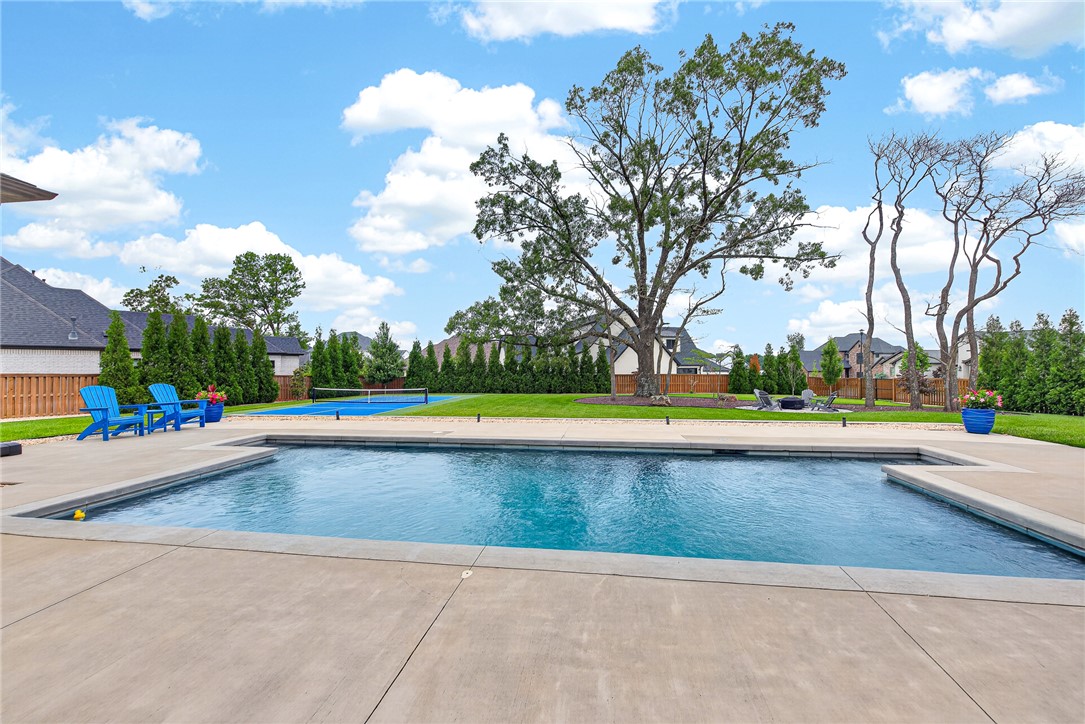 STUNNING .72 ACRE PROPERTY w/ CUSTOM-BUILT ONE-LEVEL HOME IN THE SOUGHT-AFTER GATED COMMUNITY OF SCISSORTAIL! Resort-style backyard retreat features a private saltwater pool, pickleball court, beautifully landscaped park-like grounds, and a covered patio with built-in grill and lounge area—creating the ultimate setting for relaxation and entertaining. The open-concept floor plan showcases a chef’s kitchen with double ovens, large marble-topped island, & abundant workspace. Living room offers a gas fireplace w/ custom built-ins and direct access to the patio and pool area. Spacious formal dining room is ideal for gatherings. Luxurious primary suite features a spa-inspired bath & expansive boutique-style walk-in closet. Fourth bedroom can be used for study/office. Additional highlights include white oak hardwood flooring, custom beam accents, exceptional storage, and the convenience of single-level living. Located just 10 min from Pinnacle Hills shopping, dining, & the Walmart AMP, & 15 min from downtown Bentonville.