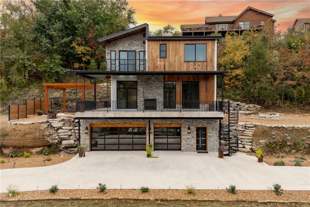 Priced below appraisal—instant equity! Both lots included. Excavated second lot—build-ready or extra parking. Perched above Beaver Lake, this modern retreat features a one-of-a-kind CAVE w/ a lounge + vault door. Glass garage doors open to lake views & stargazing—perfect for entertaining. Water views from every angle. Minutes to downtown Rogers. Boat launch 30 seconds from property. Private waterfall entry. Open living with dual-sided fireplace & full-length deck. 3 bed, 3.5 bath, finished lower level, geothermal. Don't miss this
