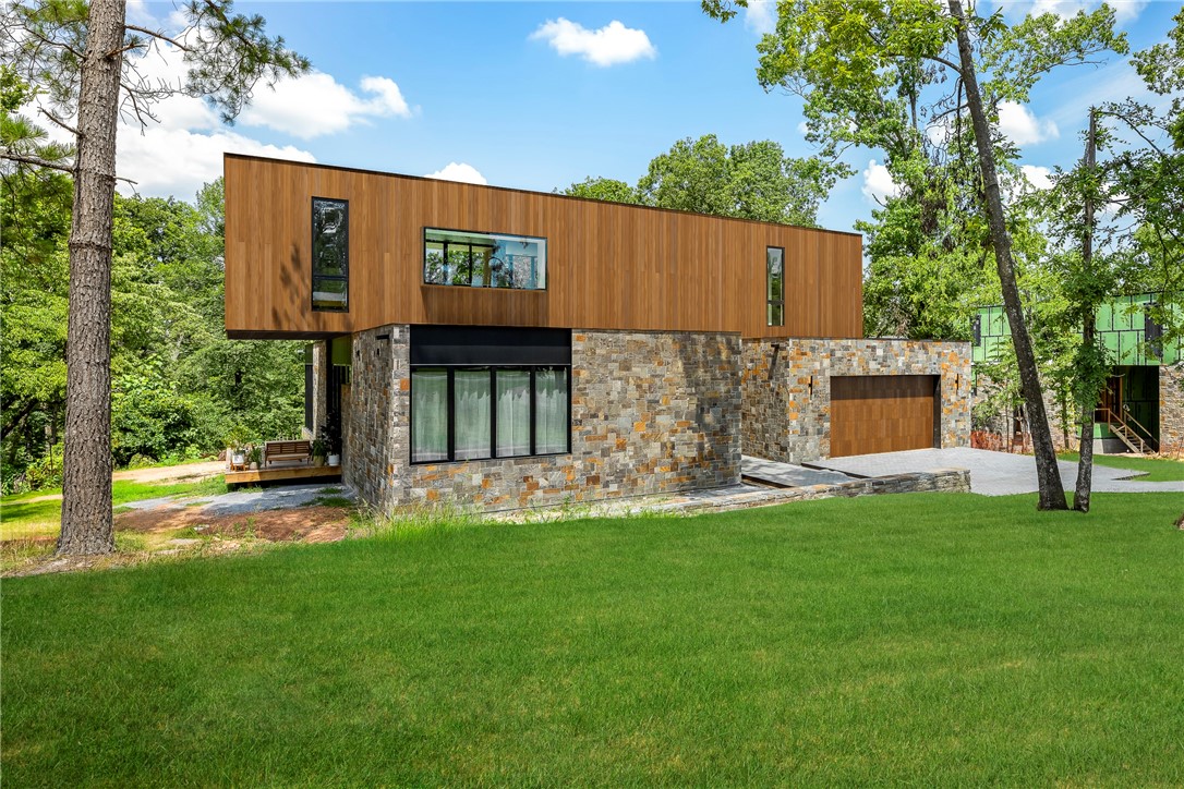 Welcome to Nelagoney Glen, an exclusive six-home modern enclave in downtown Bentonville where architecture, light, and nature align. Designed by Modus Studio, this contemporary residence was intentionally created to blend into its surroundings rather than compete with them. Set on nearly half an acre and adjacent to Park Springs Park. Floor-to-ceiling windows bathe the interior in natural light, creating a calm, sun-soaked atmosphere. Striking cantilevered architecture, natural stone, and Accoya wood siding showcase exceptional craftsmanship and material selection. The chef’s kitchen features upgraded appliances including a Fisher & Paykel 36" slide-in induction range, paneled refrigerator and dishwasher, and an oversized walk-in pantry. The primary suite is a true retreat with heated floors, a spa-like European wet room with soaking tub, and an impressive walk-in closet. Four bedrooms plus a private office or studio with its own bath.  A rare opportunity for luxury modern living in the heart of Bentonville.