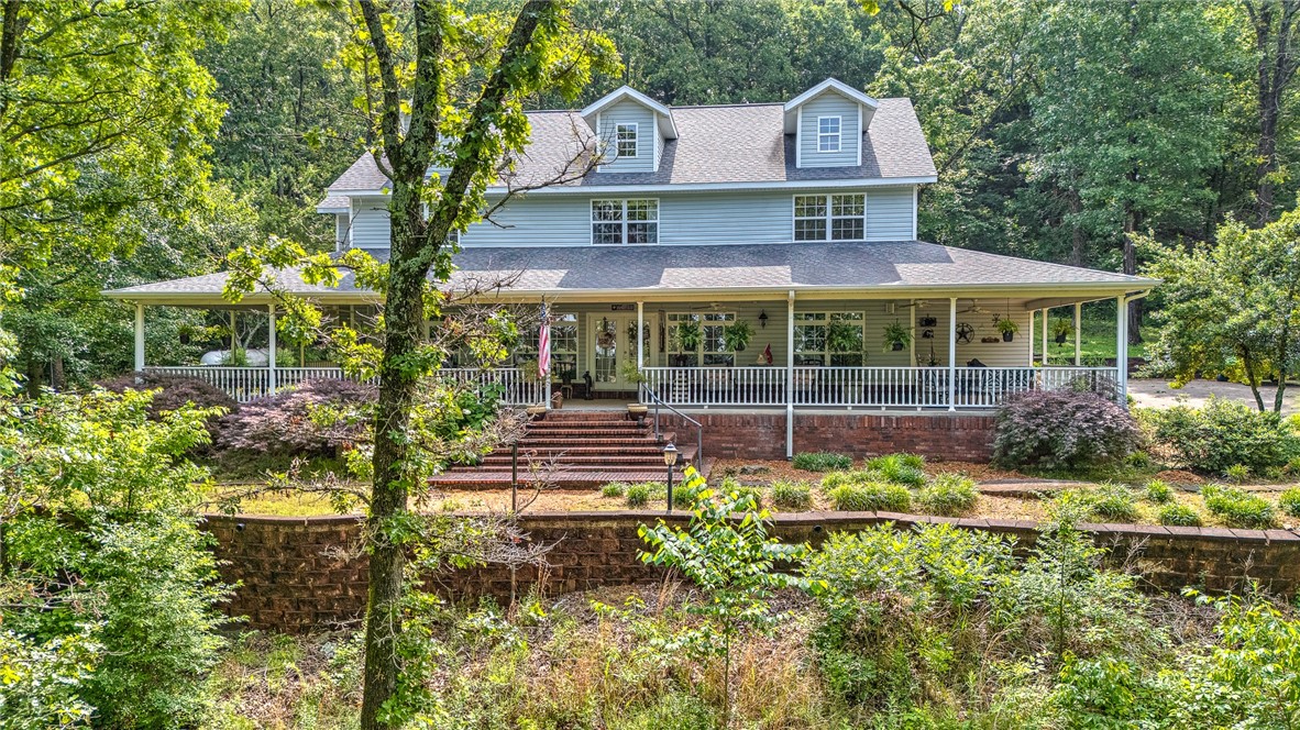 Discover this charming country farmhouse style home nestled on five wooded acres in the desirable Prairie Grove area. This spacious 3-bedroom, 3-bathroom home offers approximately 3,700 square feet of living space, complemented by a beautiful, recently remodeled kitchen (2021) featuring double ovens, a built-in freestanding ice maker, and a refrigerator that conveys. The home boasts real wood flooring throughout and two primary bedrooms, ideal for flexibility and privacy. Enjoy the privacy and tranquility of your surroundings while relaxing on the expansive 1,500-square-foot covered wrap-around porch—perfect for outdoor entertaining. Additional amenities include a heated and cooled 864-square-foot metal building (not included in the total square footage), perfect for a workshop or storage, and a long driveway lined with 25 exterior lamp posts that enhance the property's charm and security. The property offers the perfect combination of modern comforts and rustic appeal in a serene, wooded setting.