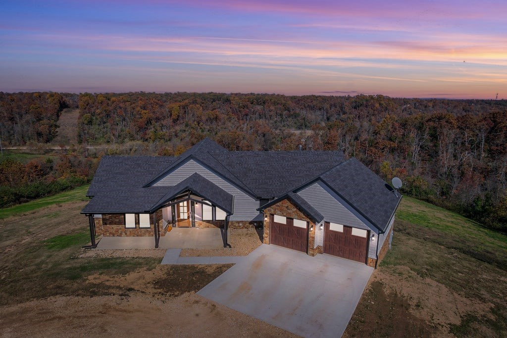 Nestled atop a serene hill on 36.92 majestic acres where deer roam and seasonal lake vistas appear, this 2023 craftsman-style home blends thoughtful design with everyday comfort. Tall ceilings and expansive windows fill the main living area with natural light, centered around a beautifully appointed kitchen. The main level offers three tranquil bedrooms and two full baths for easy, refined living. Downstairs, the walk-out lower level provides a welcoming setup for extended family or guests, complete with a full kitchen, separate laundry, a stylish bath and two bonus rooms ideal for a studio or extra-bedroom use. Located in Lowell, the home is approximately a 10–15 minute drive to I-49 and positioned near the Benton/Washington County line, offering both privacy and convenience. Immerse yourself in nature and embrace a lifestyle of seclusion and comfort.