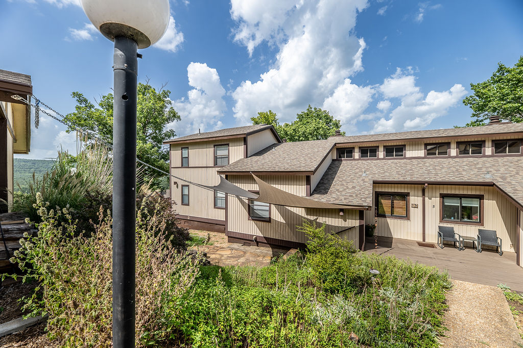 Beautifully updated 2bedroom, 2bath condominium in the highly desirable Oak Point II community of Holiday Island! This move-in ready home offers 991± sqft. of thoughtfully designed living space featuring soaring cathedral ceilings, gorgeous wood flooring, custom kitchen cabinetry, granite countertops, pantry, updated LED lighting, and an open-concept layout filled with natural light. The inviting living area features a stunning wood-burning fireplace with a custom mantel and tile surround. Relax on the covered deck overlooking peaceful surroundings or enjoy additional outdoor living on the covered porch and beautiful stone patio, perfect for entertaining. Recent updates include a roof replacement approximately three years ago, programmable thermostat, ceiling fans, double-pane windows, detached carport, and abundant storage. Enjoy Holiday Island amenities including a community pool, marina, community boat slips, lake access, golf, parks, trails, and more, all just minutes from historic downtown Eureka Springs.
