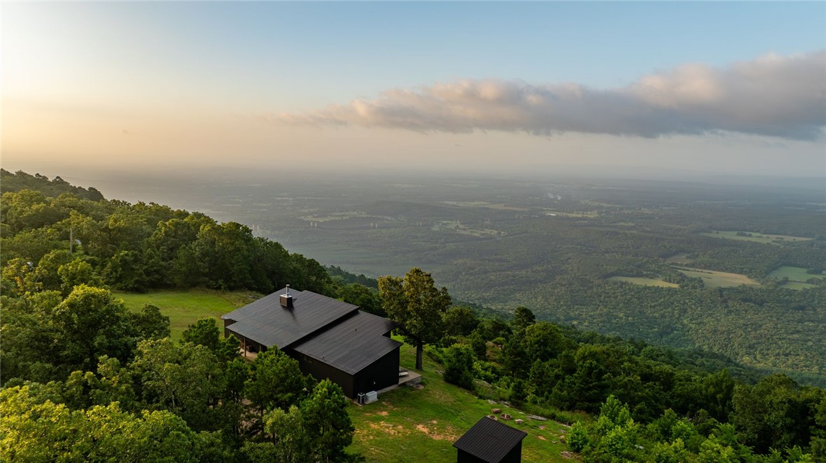 Perched atop six breathtaking bluff-top acres in the Ouachita Mountains, with direct access to a private backcountry airstrip and its own modern hangar, this extraordinary retreat offers a rare blend of luxury, privacy, and adventure. Fly directly into John Harris Field (AR05), taxi to your hangar, and be home within minutes. Built in 2019, the Scandinavian-inspired residence offers approximately 2,200 square feet with 3 bedrooms, 3 private baths, soaring ceilings, polished concrete floors, and dramatic 17-ft Marvin windows framing panoramic mountain views. The open living space, anchored by a wood-burning fireplace, flows seamlessly into a well-appointed kitchen with pantry and Sonic nugget ice maker. Designed for efficiency and comfort, the home features passive solar construction, fiber internet, a 22KW Generac generator, a private 192-foot well, Hardie Plank siding, and a standing seam metal roof.
Featured as a backcountry flying destination- a mountain escape where refined design meets the freedom of flight.