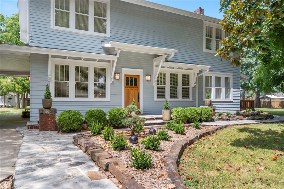 This exquisitely restored Prairie-Craftsman farmhouse—an iconic piece of Bentonville’s history—was once part of a 500-acre apple orchard. Every detail honors this home's legacy, from the original wood floors and high coffered ceilings to the wainscoting and restored double-hung windows, seamlessly paired with the confidence of a full-scale renovation, including updated plumbing, electrical, HVAC, foundation, and a new roof. The home blends timeless craftsmanship with elevated finishes, including soapstone, Carrara marble, and custom black walnut cabinetry crafted by local artisans. Expansive living spaces, spa-inspired baths, and a chef’s kitchen create a home that is as functional as it is beautiful. A vaulted coach house provides flexible space for a studio, office, or fitness retreat. With 1,200 square feet of wraparound decking, native stone patios, and lush, park-like gardens, the full-acre lot offers endless possibilities, including room for a guest house, garage, or pool.  Just minutes from the square.