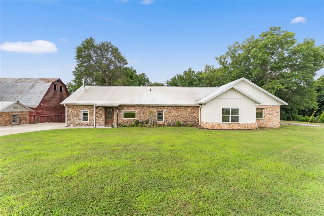 Experience the perfect blend of historic charm and modern convenience in this beautifully updated rock home situated on nearly 2 acres. The open-concept layout features a spacious living area with a stunning stone fireplace, warm wood accents, and a functional kitchen designed for everyday living and entertaining. Outside, enjoy the screened porch, hot tub, mature shade trees, and peaceful surroundings. The property’s showpiece is the iconic red barn, accompanied by an additional stone outbuilding, offering endless possibilities for storage, hobbies, workshops, or future use. Additional features include sound-insulated bedroom walls, solid wood doors, USB outlets, hot and cold exterior water access, electric service to the barn and stone shed, attic fan, trash compactor, Bluetooth speaker fan in the primary bath, hot tub hookup, and a 50-amp RV hookup. A rare opportunity to own a truly unique Northwest Arkansas property.