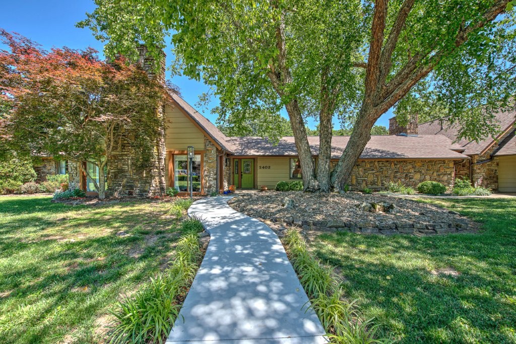 HOT LOCATION! Stone and cedar updated home on TWO LOTS TOTALING JUST UNDER 1 ACRE in Hidden Springs subdivision, ideally located between downtown Bentonville and the new Oz Trails Bike Park w/mountain bike lift. Enjoy quick access to paved and MTB trails right outside the subdivision. The great room features a soaring cathedral ceiling and a striking stone fireplace. From the hearth, look up to the double door entry of the 4th bedroom/bonus room framed by custom built ins. The open kitchen/dining/hearth room includes a 5' x 7' granite island, custom cabinetry, creamy farm sink, and cozy gas fireplace. Perfect for entertaining, the outdoor space offers a large deck, patio, fiberglass/Gunite PRIVATE POOL, and an expansive yard across both lots. Extras include multiple living/dining areas, an oversized 3 car garage, extended parking pad, mature trees, and storage shed. Stone pillars and boxwood borders create a warm welcome home.