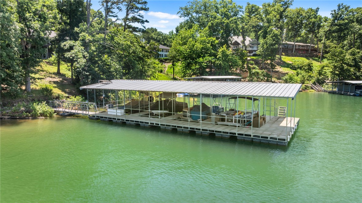 Stunning fully remodeled Lakefront home that includes two 10x24 slips with lifts in a co-owned boat dock with swim deck and an easy stroll to the water’s edge. Enjoy gorgeous lake views from every room featuring large picture windows for lots of natural light. Intimate living room is highlighted by a fireplace with gas logs and built ins or enjoy casual living in the sunroom. Beautiful kitchen with stainless steel appliances, quartz counters and center island offering sink & bar seating. Impressive updates and gleaming hardwood floors throughout main level of the home. Primary bedroom features a walk-in closet and separate sitting room overlooking the lake as well as a spa like bath with walk in shower. Additional guest suite and full bath complete the main level. The lower level boasts a family room with wood burning fireplace, full bath, two more guest suites and great flex space. Step outside on the deck or the lower-level covered patio great for entertaining and taking in the sunsets. Roof & Hot water tank 2026