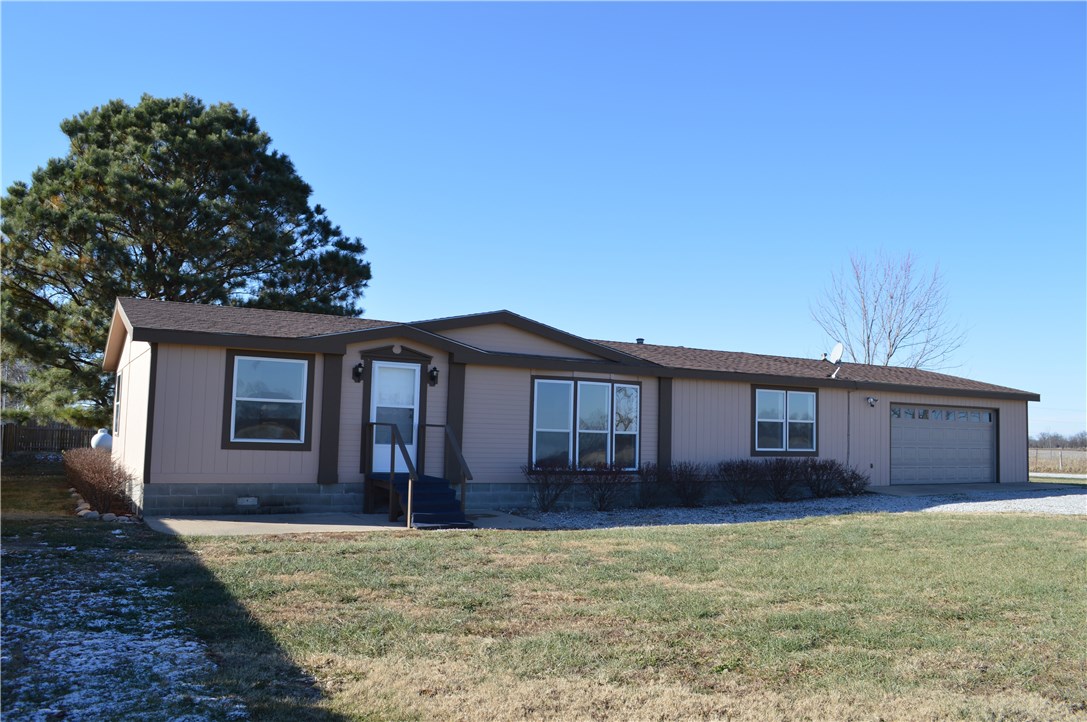 Country living at an affordable price! 3 bd, 2 ba double wide mobile home has 1,456sf & sits on .81 acre, with rural water. New carpet & paint, several new light fixtures & new vinyl flooring in kitchen, dining & utility areas. Open floor plan boasts large living area & tons of natural light. Kitchen has a great amount of storage space & a separate pantry. On demand hot water heater. Attached oversized 2 car garage with additional storage. Property is fenced with mature trees.