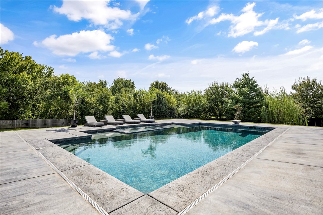 Discover unmatched luxury in this 7,600+ sq ft modern masterpiece in Bentonville’s prestigious St. Valery’s Down. A striking stucco-and-stone exterior with standing seam metal roof sets the tone. Step inside to soaring two-story spaces, a dramatic living room with a horizontal fireplace wrapped in shou sugi ban wood and metal, and walls of glass opening to the resort-style patio. The chef’s kitchen boasts an oversized island, Wolf 8-burner gas cooktop, and built-in refrigeration. Entertain in the pool room with full bar, pool table, and surround sound, or retreat to the theater. Outdoors, a heated saltwater pool with tanning ledge and infinity spa delivers a private resort experience. Every bedroom offers an ensuite bath, while whole-home audio, app-based automation, and tongue-and-groove porch ceilings elevate daily living. Sophisticated, bold, and designed for both grand entertaining and intimate relaxation—this estate is Bentonville living at its finest.