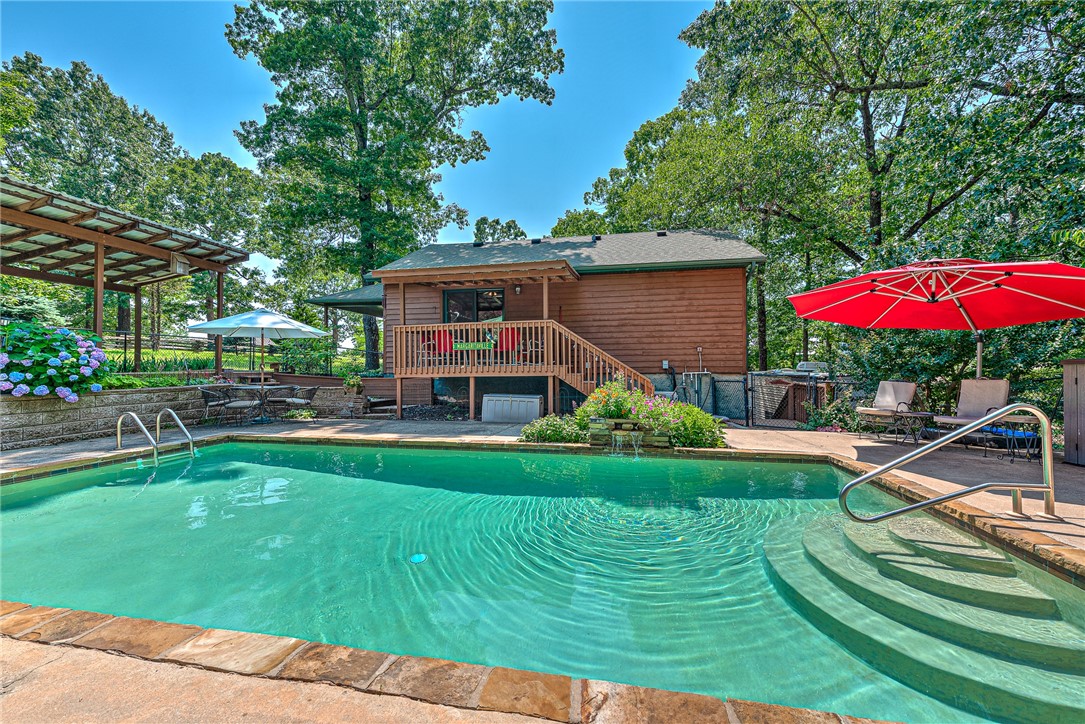 RUSTIC RETREAT FEATURING MAIN HOME, GUEST HOUSE, POOL, WORKSHOP ON 2.78 PEACEFUL ACRES. Near Beaver Lake’s Rocky Branch, every detail of this lodge style home has been thoughtfully crafted. The main home showcases custom doors, built-ins, real antler chandeliers, and wood-burning fireplaces. Downstairs offers a cozy pub, full bath, and workshop—ideal for entertaining or hobbies. A spacious 4-car garage with an extra roll-up door provides ample storage, and a whole-home Generac generator ensures year-round peace of mind. The guest house/in-law suite includes pine floors, a full kitchen, and private patio for extended stays. The attached heated/cooled shop has a half bath and potential for additional living space. Outdoor amenities include a solar-heated sport pool, hot tub, plumbed outhouse, turfed bocce ball court, RV parking, and lush landscaping filled with perennials and native plants. This one-of-a-kind property blends comfort, craftsmanship, and outdoor luxury.
