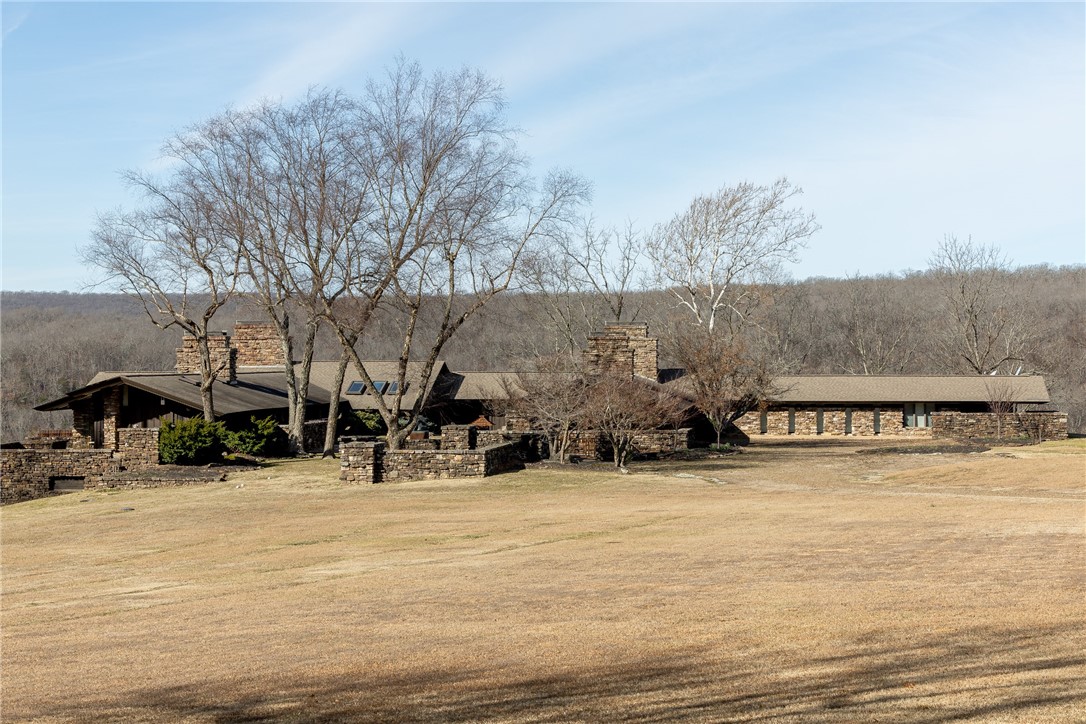 Architecturally significant estate designed by one of NWA's most renowned architects, offering a rare opportunity to own a true work of art. Built in 1976, this stone & cedar residence features 6,333 sq ft, vaulted ceilings with exposed beams, extensive flagstone floors, walls of glass, skylights & seamless indoor/outdoor living. Four massive stone fireplaces anchor the home, complemented by custom wood lighting, built-ins & rich natural materials throughout. Kitchen offers quartz counters, bar seating & high-end stainless appliances. Primary suite includes fireplace & dual baths. Guest quarters functions as a private “house within a house.” Outdoors enjoy a gunite pool with waterfall & courtyard gardens framed by stone walls & metal gates. Gated 806 acres includes 10 ponds, White River frontage, cross-fencing, second home, horse barn, hay barns & equipment buildings, offering exceptional equestrian, farm or recreational potential. A rare legacy estate where architecture, privacy & panoramic views come together.