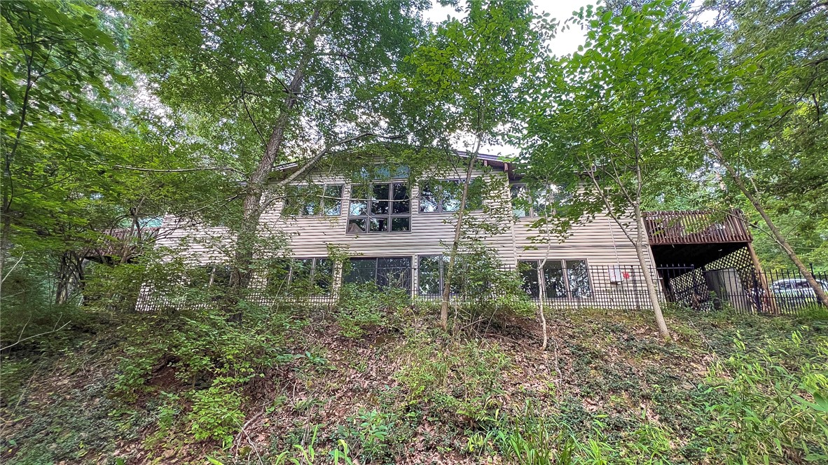 This charming, custom-built, one-owner home is tucked among the trees, offering privacy while remaining convenient to highway corridors, schools, grocery stores, restaurants, and shopping. Large windows fill the home with natural light, while beautiful wood bookshelves and native stone fireplaces add warmth on both the main and lower levels. The main level features an open-concept living, dining, kitchen, half bath, and sunroom area, plus an office/bedroom and the primary bedroom/bath. The lower level includes a second den with fireplace, two bedrooms, one bathroom, and a storage/workout room. Additional highlights include a new roof in 2026, Pella windows, two storage sheds, and solar panels & 14' swim spa that convey with sale. This home is an ideal fit for buyers seeking a peaceful, secluded setting with everyday conveniences nearby.
