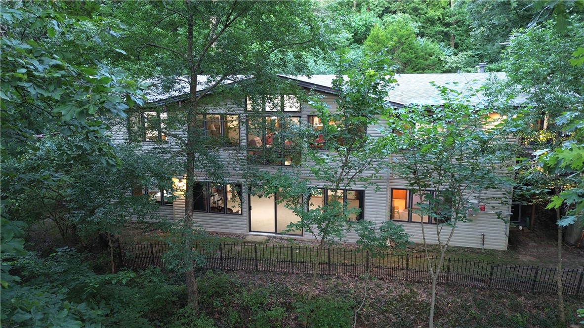 Secluded woodland retreat on 5.6 acres in East Fayetteville, architect-designed, custom-built, 1-owner post-and-beam home offers rare character, privacy, modern efficiency. Disguised by foliage yet minutes from shopping, dining, medical services, & schools. Low-E Pella windows allow natural light & wooded views, while vaulted wood ceilings, exposed beams, oak-mahogany-clad posts, native stone fireplaces, and custom built-ins add stylish warmth. Main level features open LR/FDR, sunroom, office/guest BR, primary suite, porch, pergola. Walkout lower level offers 2nd family room w/FP, 2 BRs, FB, and storage/gym space. Quality features: solid-core doors, insulated interior walls, solid wood/plywood construction, R-27 roof, dual HVAC, hot-water recirculation, fiber internet, solar panels reducing electric costs about 35%. Newer updates: 2026 30-year roof, upstairs HVAC, engineered hardwoods, new kitchen appliances. Outdoors: swim spa, gazebo, 2 storage buildings, playhouse, nature trail, parking w/turnaround.