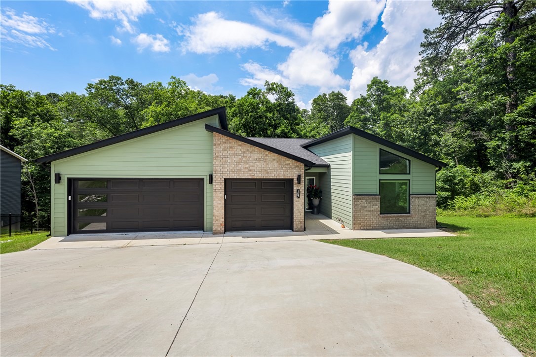 Modern style meets wooded privacy in this like-new 4 bed, 3 bath home that includes an office and a striking exterior that stands out from the rest. Tucked away on a secluded wooded lot, this home offers sleek finishes, tall ceilings, and spacious living areas throughout. The main level features open-concept living, a guest bedroom and full bath, plus a large primary suite with dual vanities, specialty lighting, oversized walk-in shower, soaker tub, and direct access to the laundry room with cabinets and workspace. Downstairs offers 3 additional bedrooms, a full bath, a large bonus area with a second fireplace, and access to a second covered deck that mirrors the upper deck. Enjoy low-maintenance outdoor living, a finished storage room perfect for seasonal decor, and a 3-car garage. Stylish, functional, and move-in ready. Schedule your tour today!