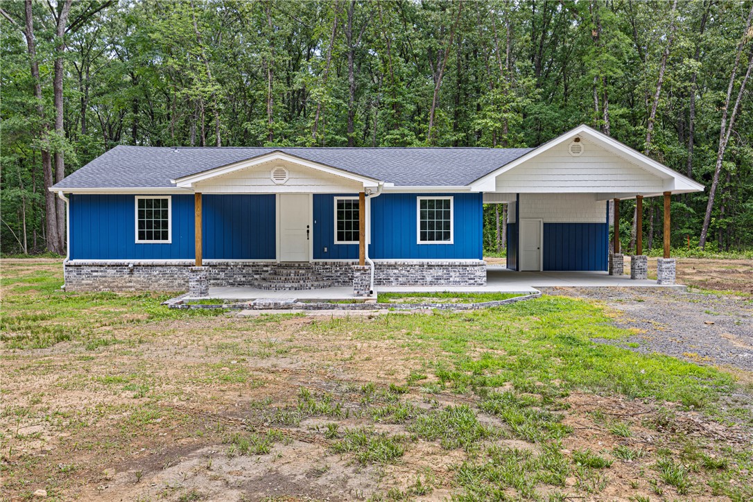 Ranch home on a wooded 1± acre lot with paved Hwy 64 frontage. Navy board-and-batten exterior with white gables, brick skirt, covered front porch, and an oversized attached carport. Open-concept main living with wood-look LVP flooring, soft blue-gray walls, recessed lighting, and ceiling fans throughout. Kitchen features stained upper cabinets paired with custom blue lowers, white quartz countertops, subway tile backsplash, matte black fixtures, walk-in pantry, and a full stainless appliance package. Back wood deck with cattle-panel railing overlooks shaded hardwoods. Includes a wired metal shop building on concrete pad and a separate storage shed. Minutes to I-40, Atkins, Russellville, and Lake Atkins.