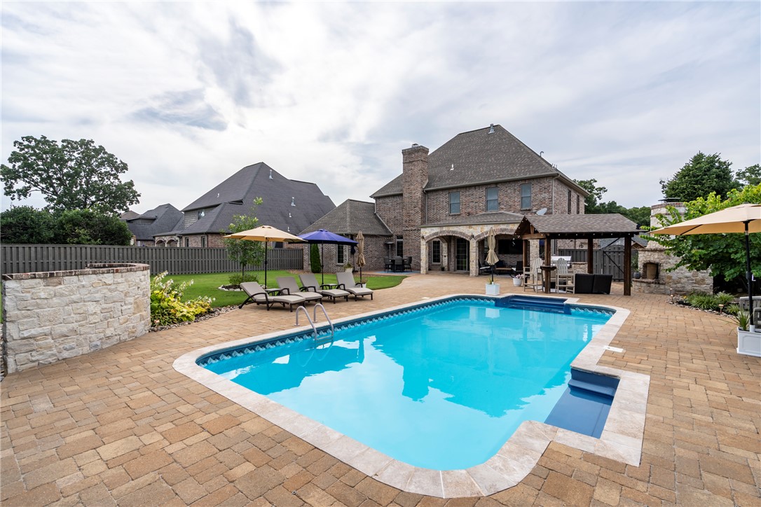 Luxury living in the gated Oak Tree Subdivision! This custom 5BR, 4BA, 4,300SF home sits on a professionally landscaped .38-acre lot. Backyard features a heated saltwater pool, wood-burning fireplace w/pergola,built-in grill,covered patio w/outdoor TV & extended stamped concrete entertaining space. Inside, you'll find a chef's kitchen w/oversized island, professional gas cooktop, butler's pantry w/wine chiller & exquisite walk-in pantry. The primary suite offers a walk-in tile shower, soaking tub,dual vanities & custom cabinetry. Upstairs has 2BRs w/Jack & Jill bath, a 3rd BR w/ensuite bath. Hardwood flooring, carpet & tile in wet areas. Spray foam insulation, surround sound, central vac, ADT security, 4-zone climate control, Generac home generator, media room w/wet bar, bonus room, & walk-in closets throughout. The insulated 3-car garage has an epoxy floor, slat wall storage system w/custom cabinetry & in-floor storm shelter. Exceptional craftsmanship & luxury amenities make this one of Centerton's premier homes.