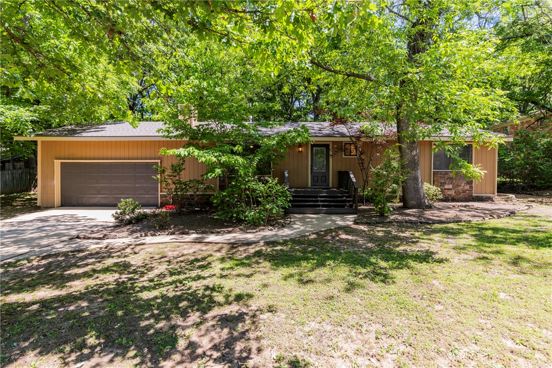 Tucked beneath a canopy of mature oaks just minutes from the University of Arkansas, this charming 3-bed, 2-bath ranch offers 1,590 sq ft of character and comfort in one of Fayetteville's most established neighborhoods. The stone-accented exterior, curved walkway, and lush natural landscaping create curb appeal with a wooded, private feel. Inside, hardwood floors anchor a warm living room featuring a stone fireplace and natural light pouring through oversized windows. The kitchen and dining area open to each other with tile floors, white cabinetry, center island, stainless appliances, and French doors leading directly to the back deck, perfect for  entertaining. There’s even a great office/bonus room.  A standout primary bedroom features dramatic black custom built-in bookshelves, a moody design that photographs beautifully! Step out back to a sprawling deck built around a mature oak tree, overlooking a fenced yard with room to play. Walk to class, Dickson St., Razorback games and all the energy of campus life.
