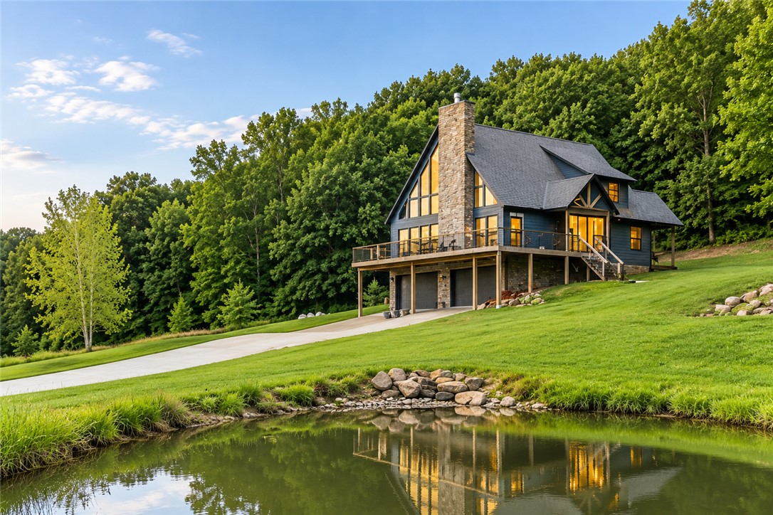 Perched atop Kessler Mountain on more than 8 private acres, this custom mountain retreat offers breathtaking sunrise views, exceptional privacy and minutes from Fayetteville. Designed to embrace the surrounding landscape, the home features soaring walls of glass, abundant natural light and a dramatic floor-to-ceiling stone fireplace anchoring the main living space. The open layout includes a beautifully appointed kitchen with a large island, custom cabinetry, granite countertops, premium appliances and walk-in pantry. The main level offers approximately 2,611 sq ft of finished living space, including a private primary suite with spa-inspired bath and custom walk-in closet. An additional approximately 900 sq ft lower-level/garage flex space is heated and versatile, ideal for gym, workshop, studio, hobby room, or additional storage. Wraparound decks, private pond, abundant wildlife, detached shop, and oversized four-car garage complete this one-of-a-kind mountain property.