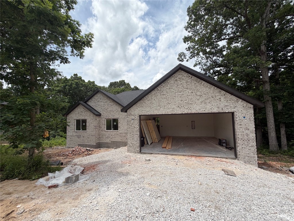New construction in the Highlands near Lake Loch Lomond with convenient access to the bypass. Estimated completion date is mid-July. Get under contract early for the opportunity to choose some finishes and add upgrades. Located in the Gravette school district. This split floor plan offers 2 bedrooms plus an office and an oversized 2-car garage. The main living area features vaulted ceilings with beams, a stacked-stone fireplace, and wood flooring throughout the main areas, hallway, and primary bedroom. Bedroom two and the office have carpet flooring. The primary bath includes a dual vanity, tiled shower with two shower heads, a linen closet, and a separate toilet area for added privacy. Exterior features include brick front with vinyl siding on the sides and back, plus a covered deck perfect for relaxing outdoors. Septic system is designed for two-bedroom capacity.
