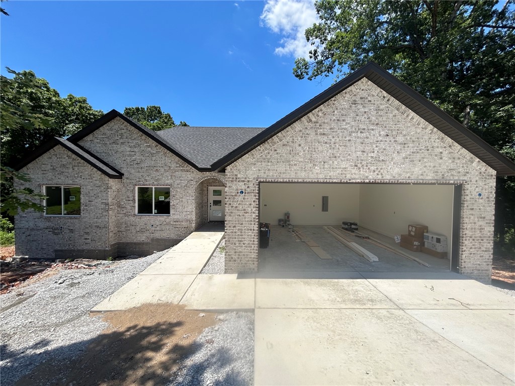 New construction in the Highlands near Lake Loch Lomond with convenient access to the bypass. Estimated completion date is mid-July. Get under contract early for the opportunity to choose some finishes and add upgrades. Located in the Gravette school district. This split floor plan offers 2 bedrooms plus an office and an oversized 2-car garage. The main living area features vaulted ceilings with beams, a stacked-stone fireplace, and wood flooring throughout the main areas, hallway, and primary bedroom. Bedroom two and the office have carpet flooring. The primary bath includes a dual vanity, tiled shower with two shower heads, a linen closet, and a separate toilet area for added privacy. Exterior features include brick front with vinyl siding on the sides and back, plus a covered deck perfect for relaxing outdoors. Septic system is designed for two-bedroom capacity.