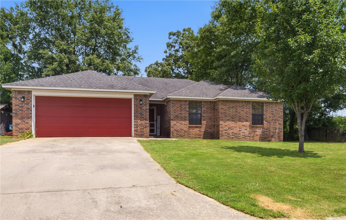 Brick 3-bedroom, 2-bathroom home with a living room featuring vaulted ceilings and a wood beam accent, opening into the kitchen and dining area. The kitchen includes ceiling-height cabinetry and stainless appliances. The primary suite has a walk-in closet with a single-sink vanity and tub/shower combo. Two additional bedrooms share a second full bathroom. Mature trees shade the yard, and there's a covered entry at the front. Set on a .19-acre lot with a 2-car garage and driveway parking, close to local schools.